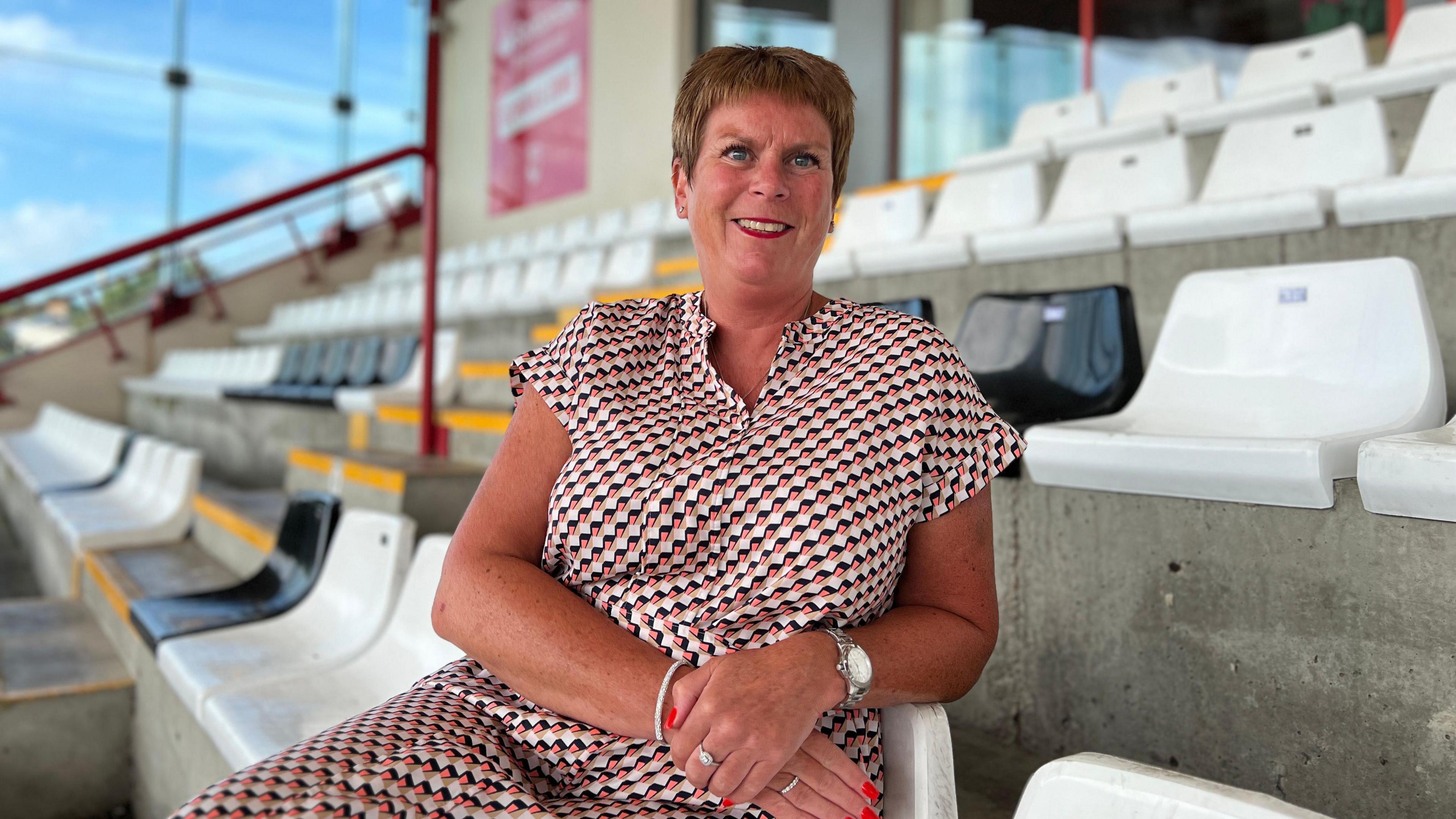 Kerrie smiles at the camera as she sits in the stand