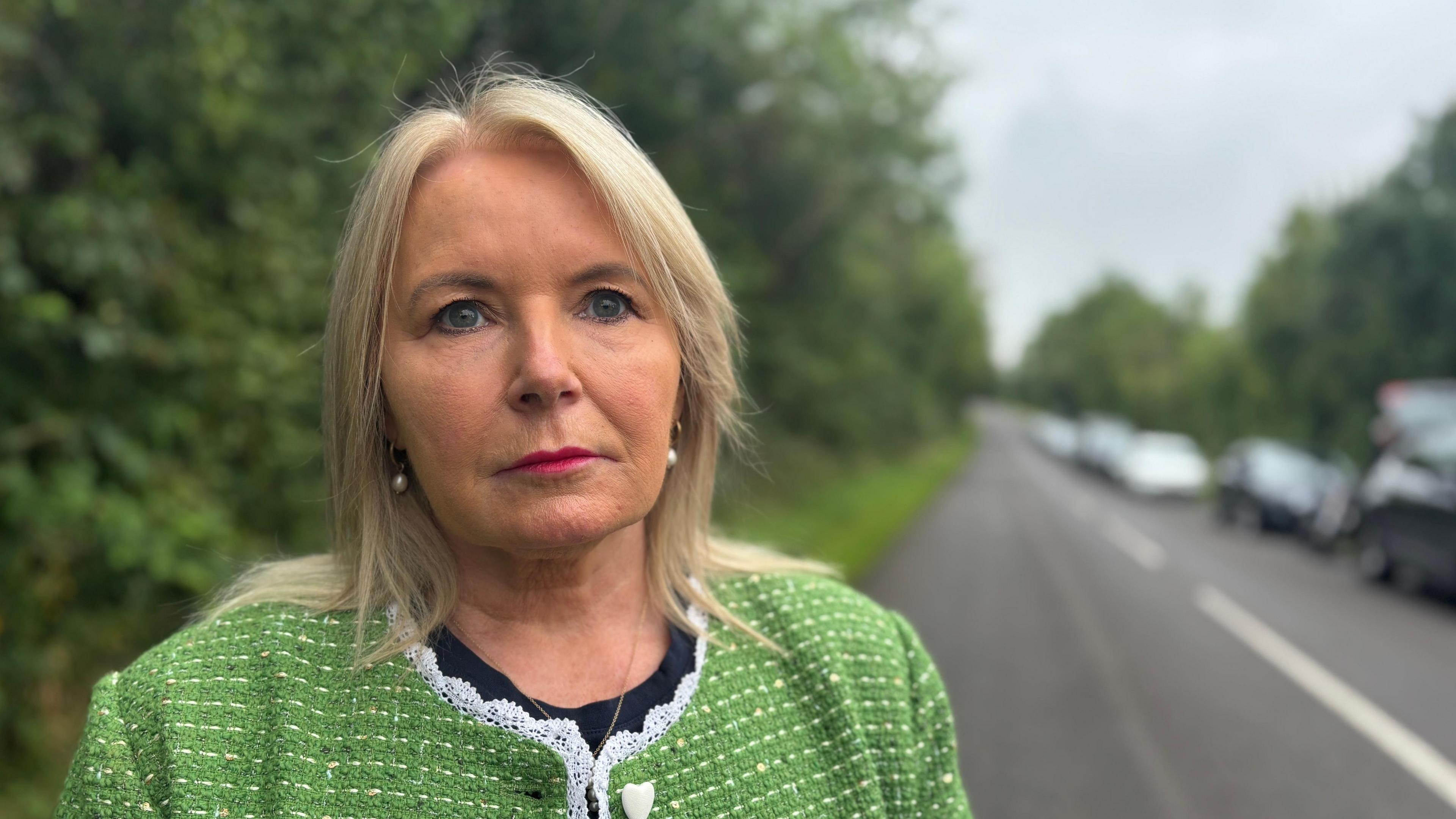 Pat Cullen. She has shoulder length blonde hair, wearing pearl earrings and green tweed cardigan.