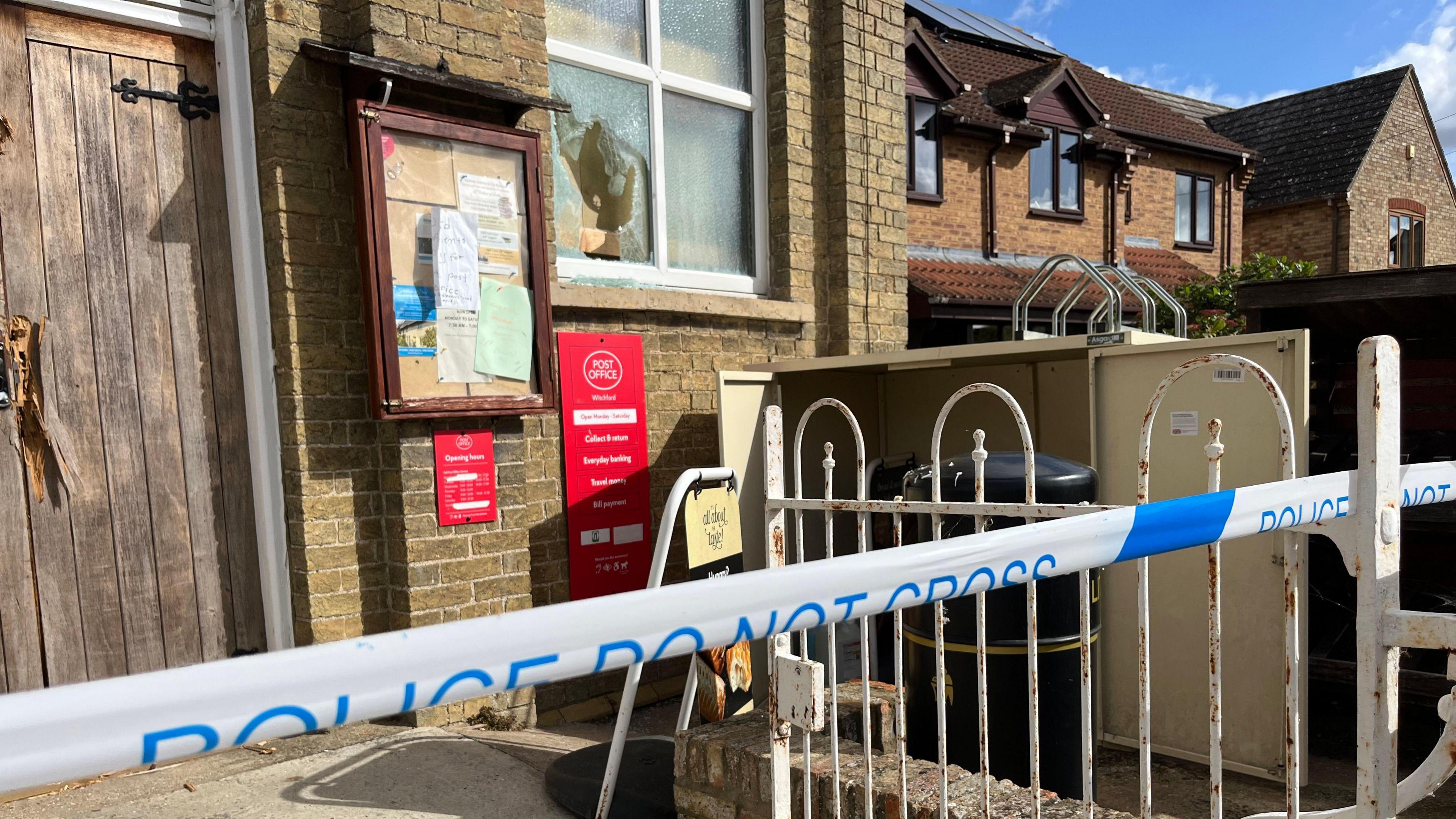The front of the post office, which has been taped off by a police cordon. The window has been smashed and the front of the wooden door appears to have been smashed inwards near the handle - but only in one part as the rest remains intact.