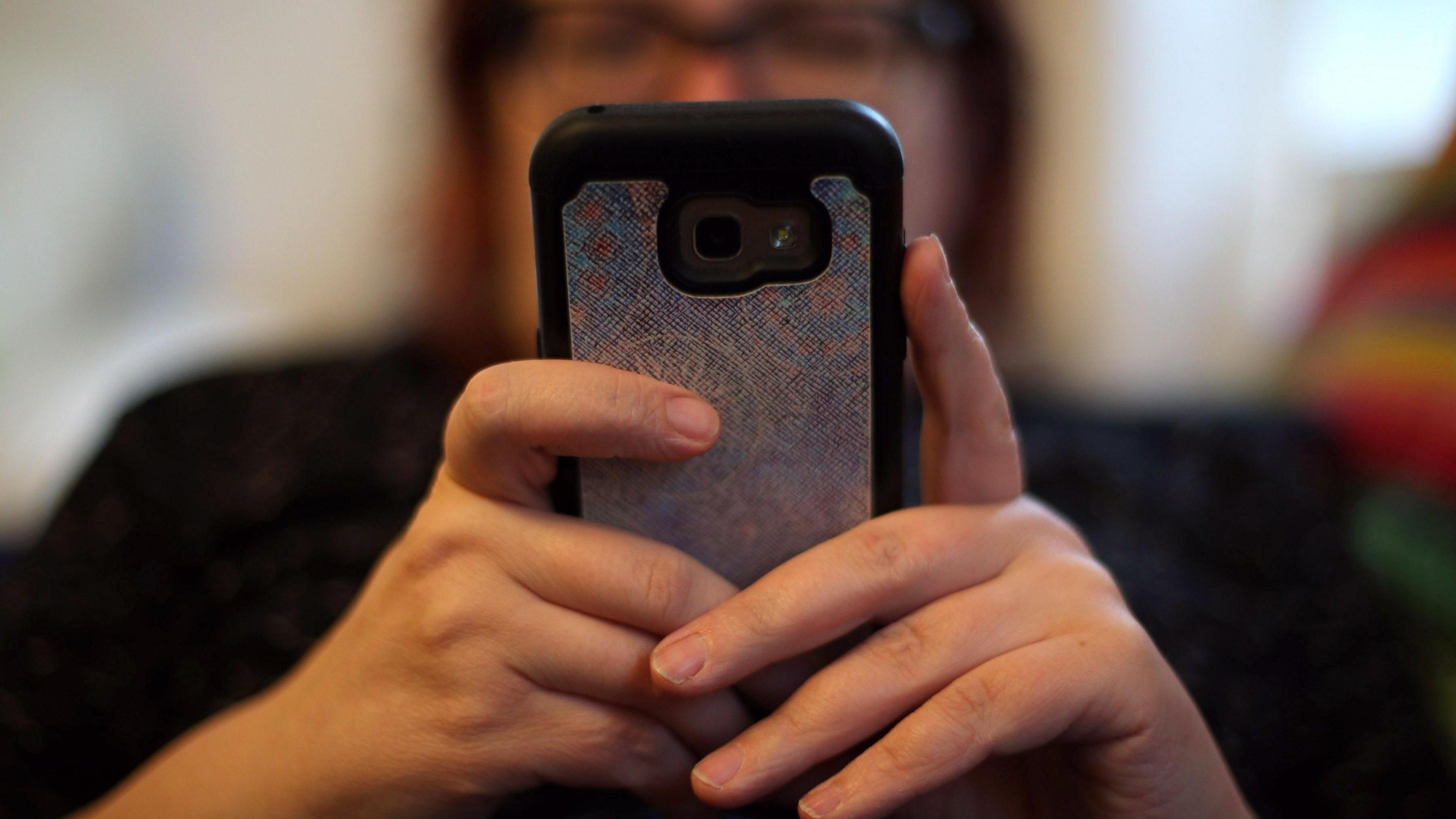 A woman holds a mobile phone up in front of her face