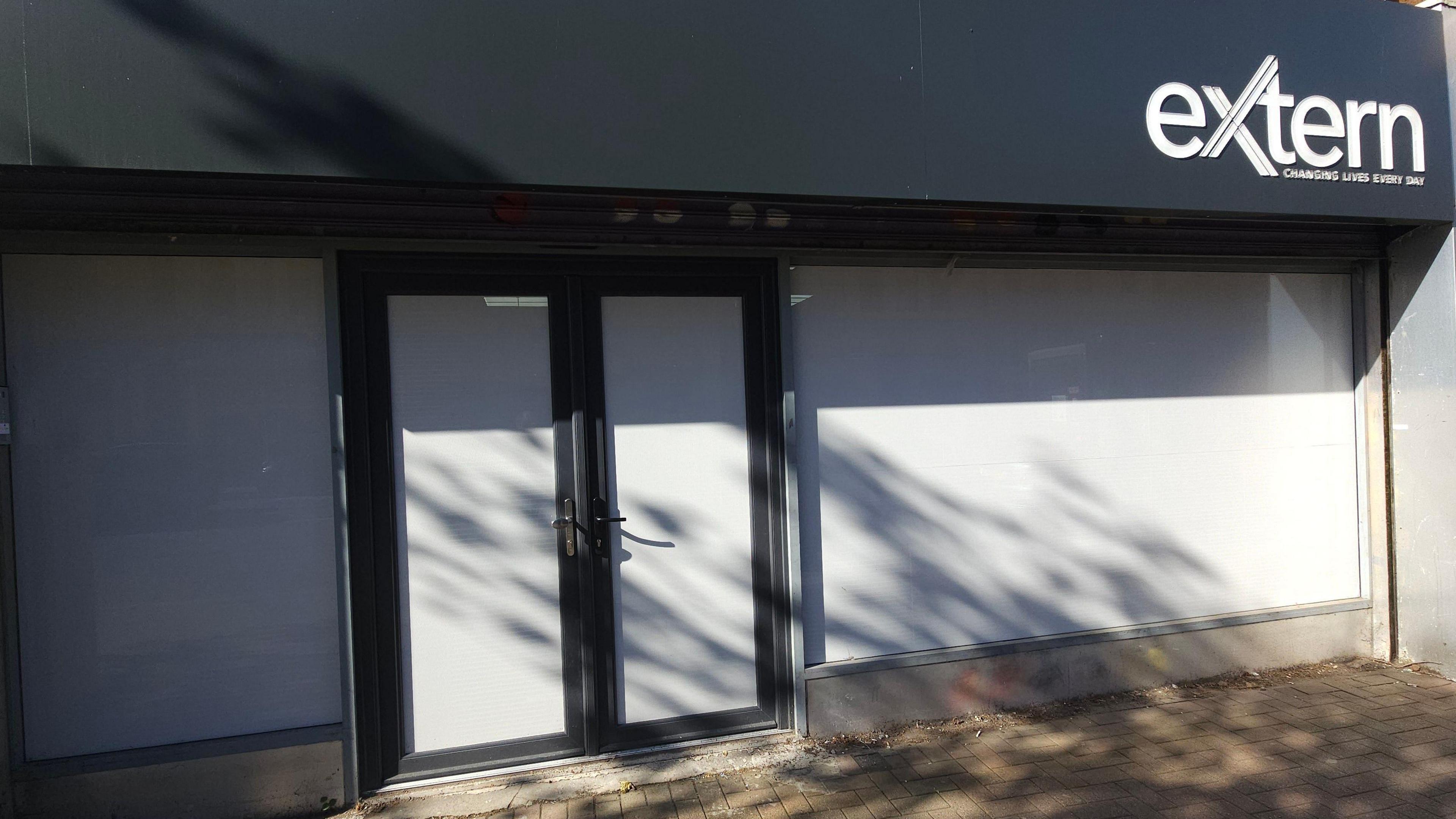 The Extern building from the outside entrance. It has navy writing on it with 'Extern' written in the top right hand side in white writing. The shutters are white and the door is black. 