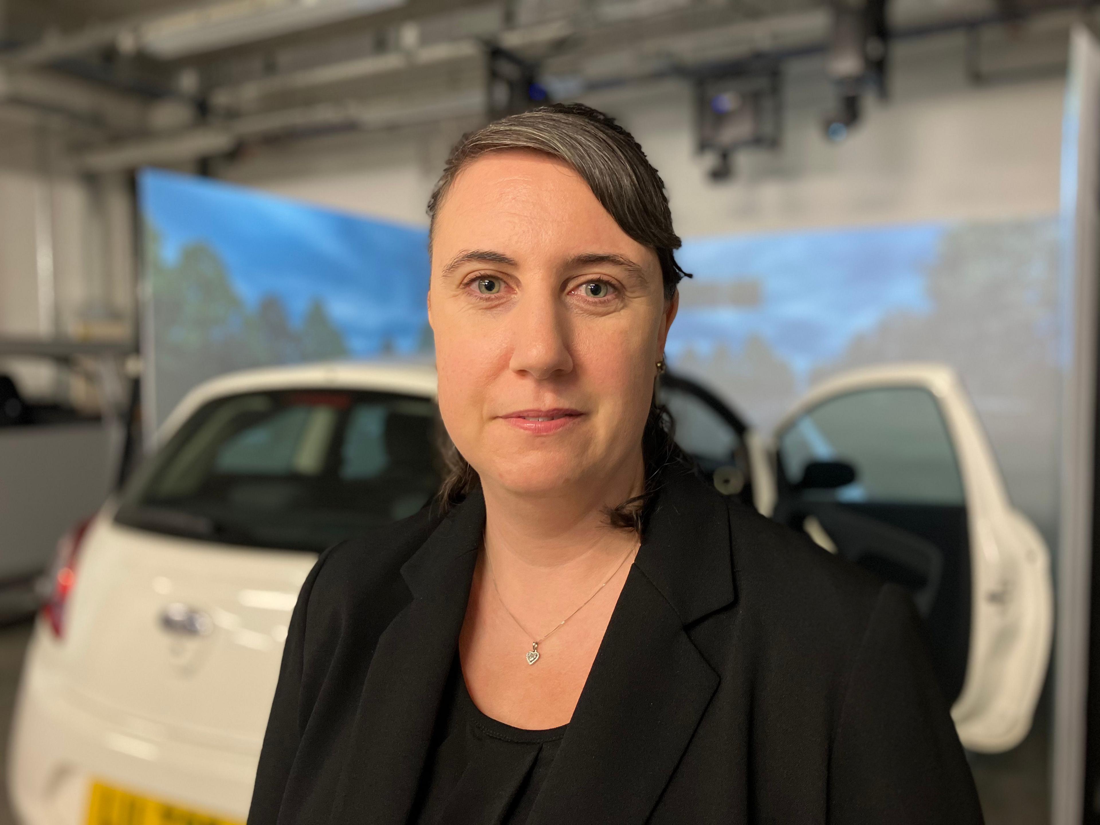 A woman standing in front of a car diving simulator