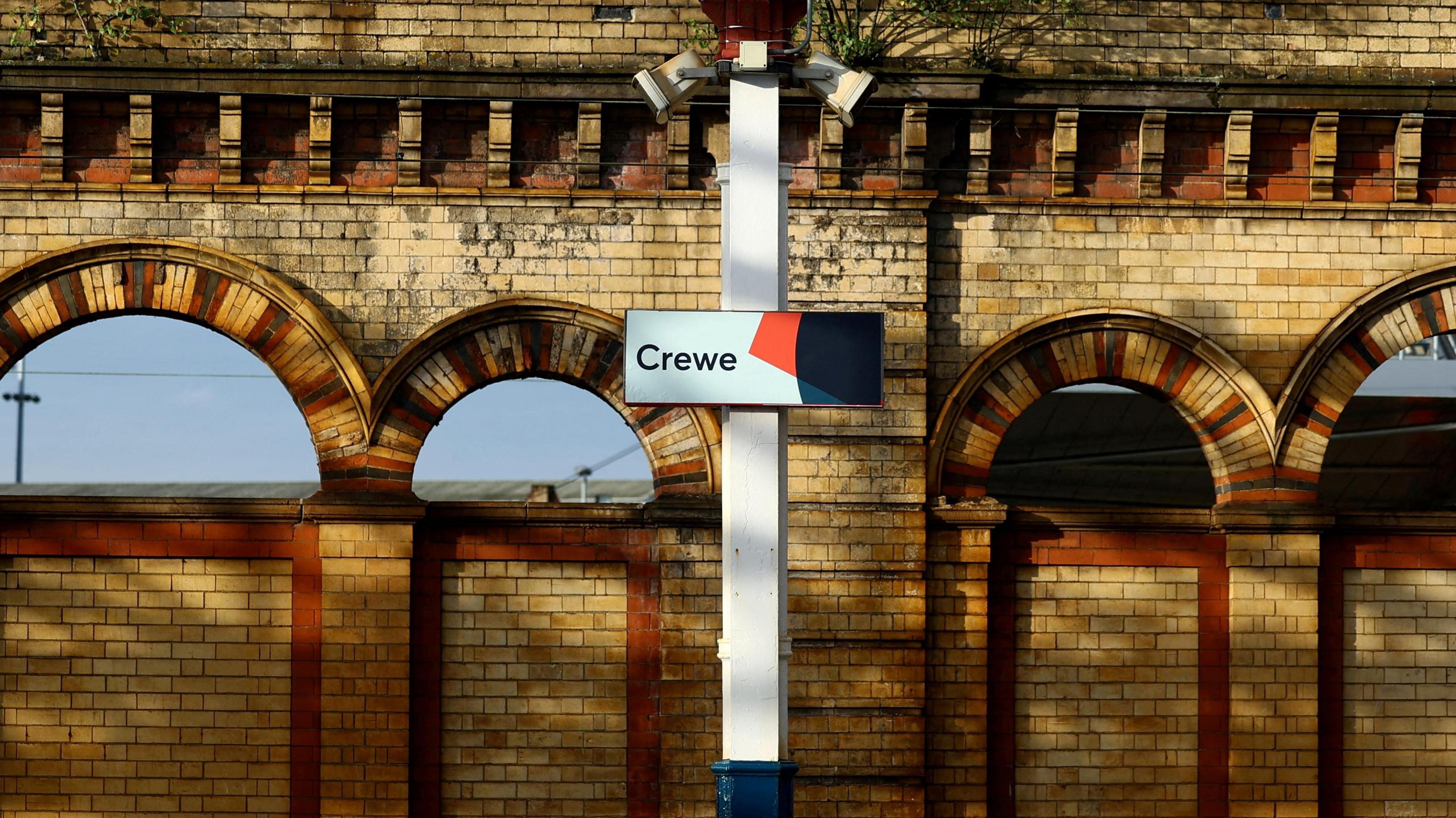 A platform on Crewe station, showing a sign on a pillar in front of Victorian brick arches. 