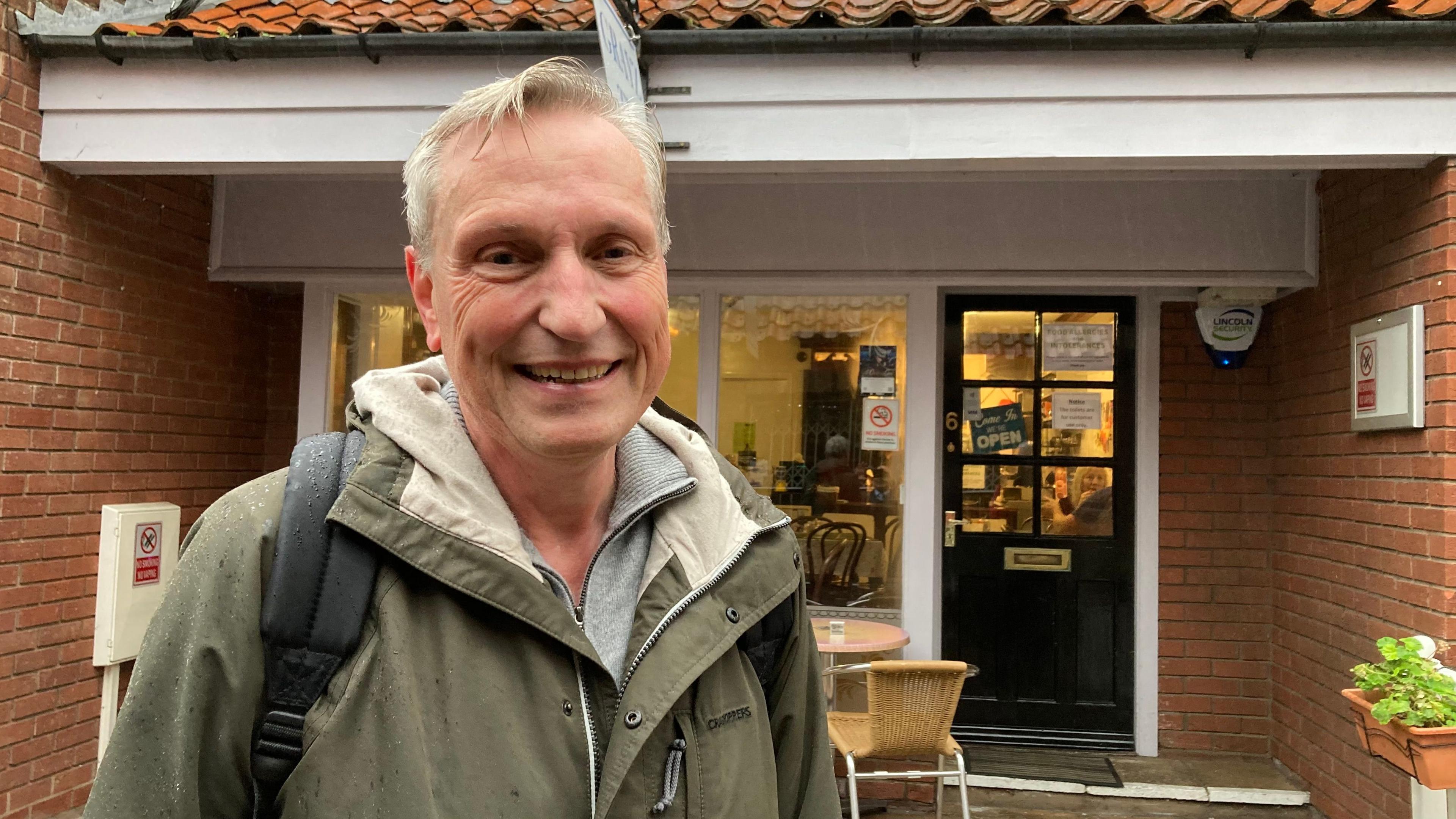 Dieter Krapp wearing a green jacket with a black bag on his back, smiling at the camera