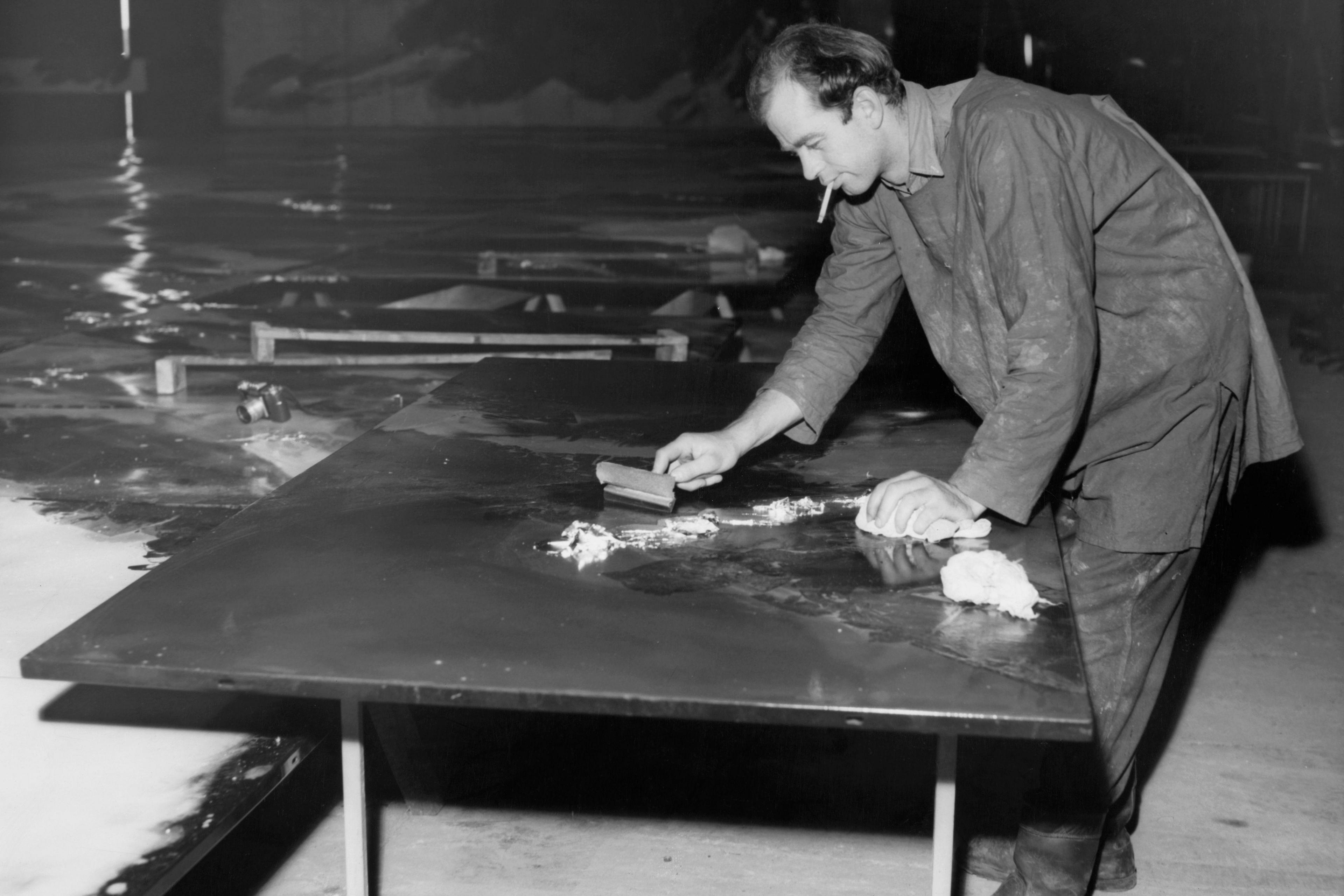 Black and white photo of Charles Lutyens leaning over a desk while smoking