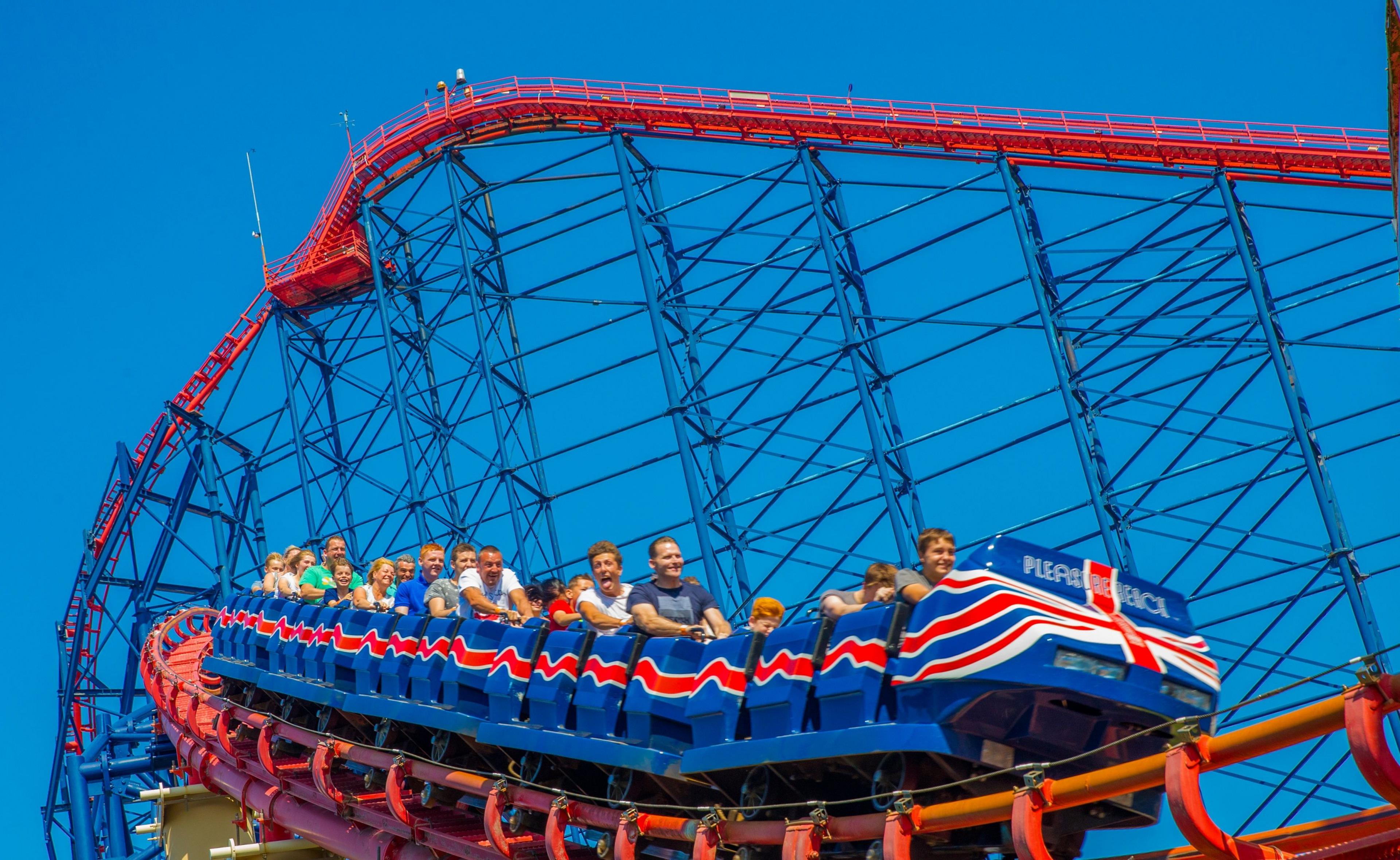 A crowd of people on a rollercoaster, which features blue and red train carts. It is a summers day 