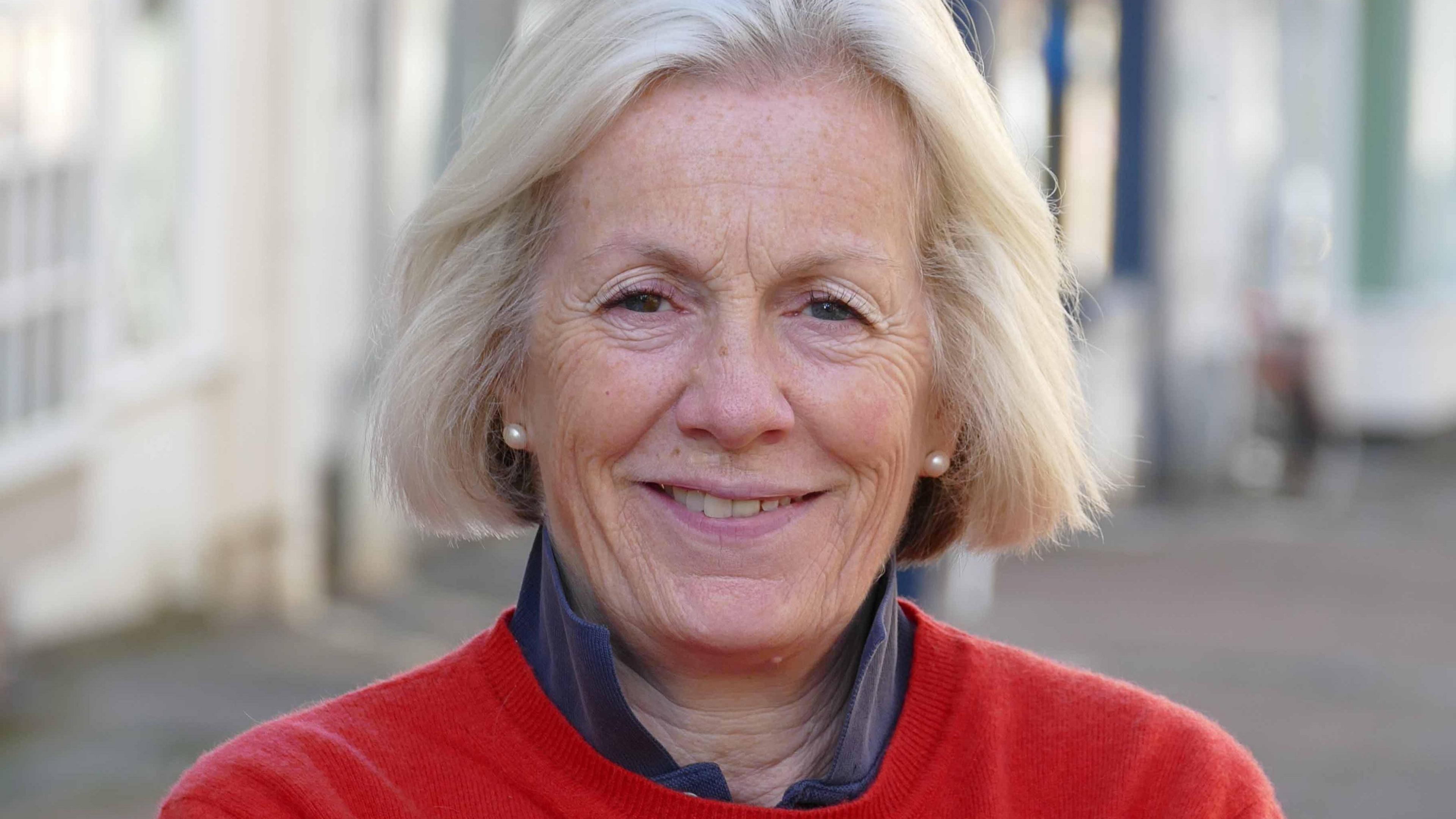 Tessa Munt smiling and wearing a red top in a street