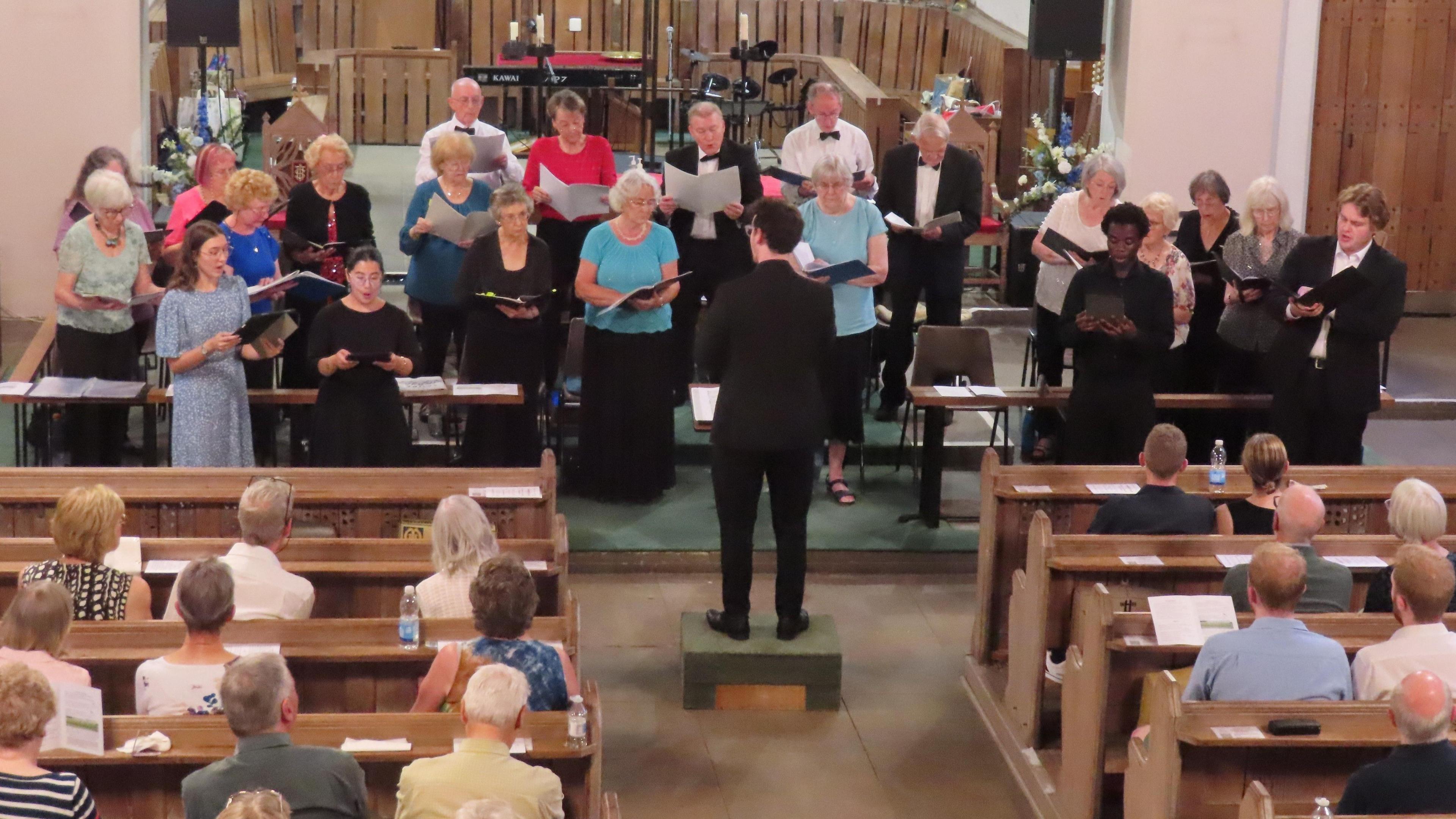 Choir singing a song at a concert at a church. Church pews are packed with the audience listening to the performance.