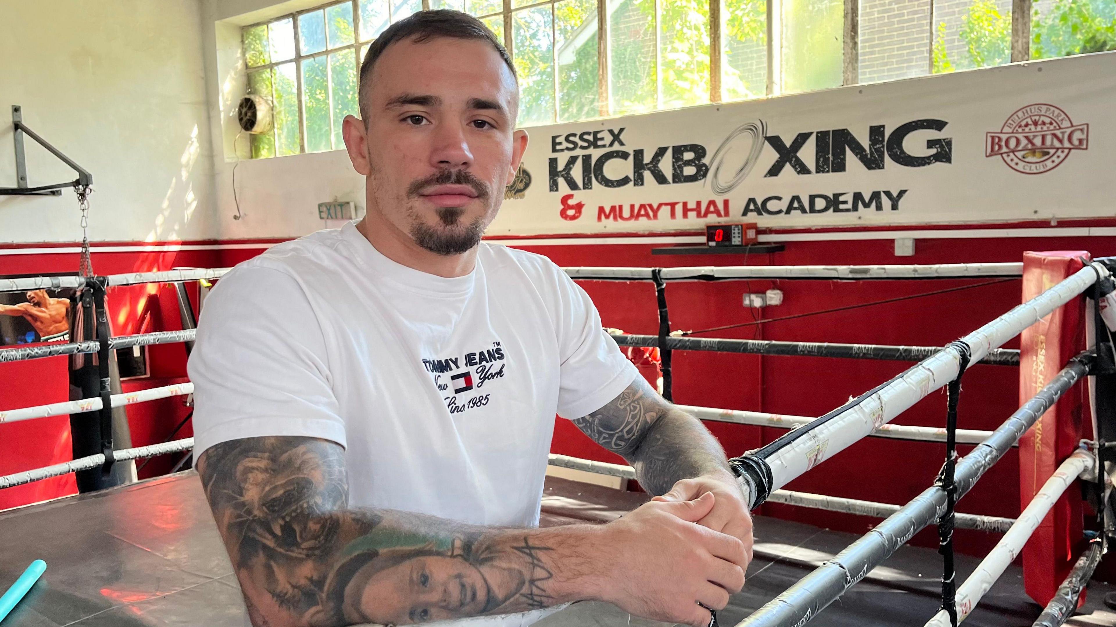 Amansio Paraschiv looks directly at the camera as he leans on the ropes at the side of a boxing ring