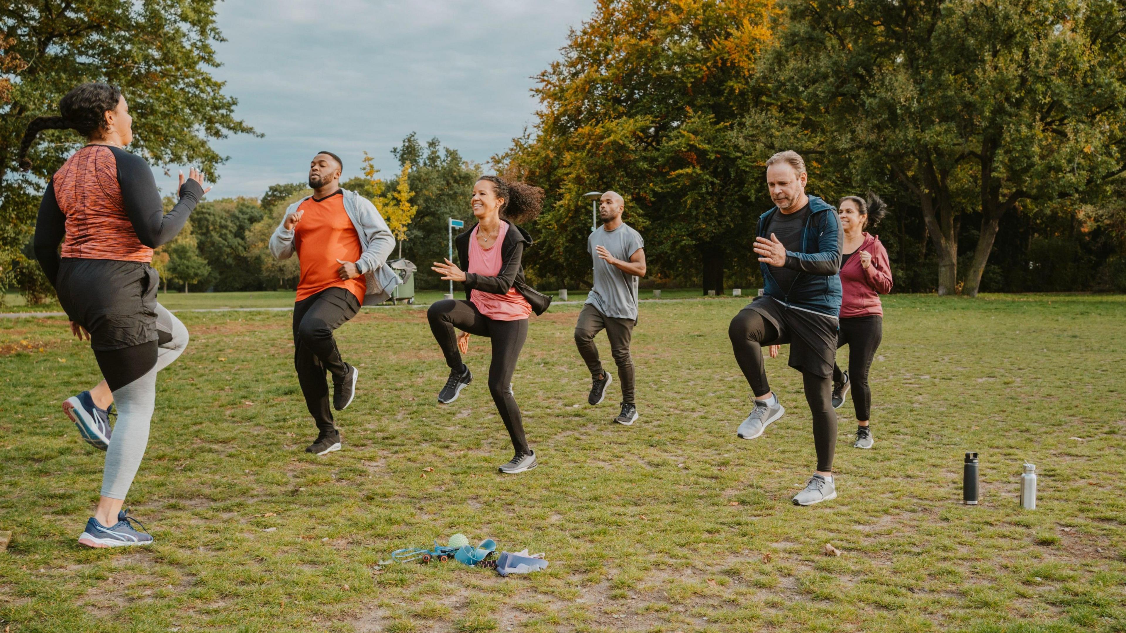 Five people running on the spot in a park, being led by a female trainer.