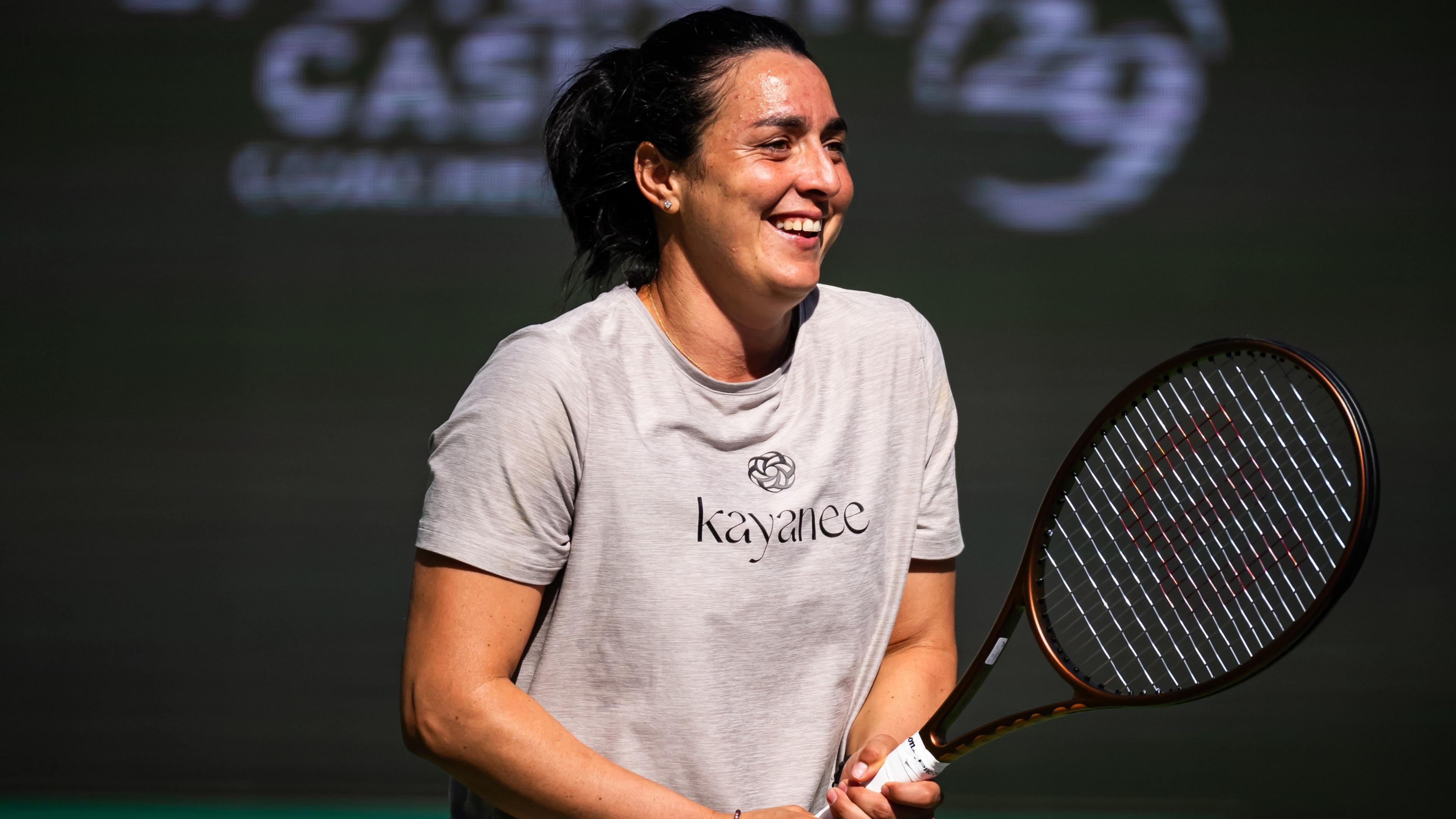 Tunisian tennis star Ons Jabeur in a t-shirt, smiling and holding her tennis racket in front of her on the practise courts at Indian Wells.