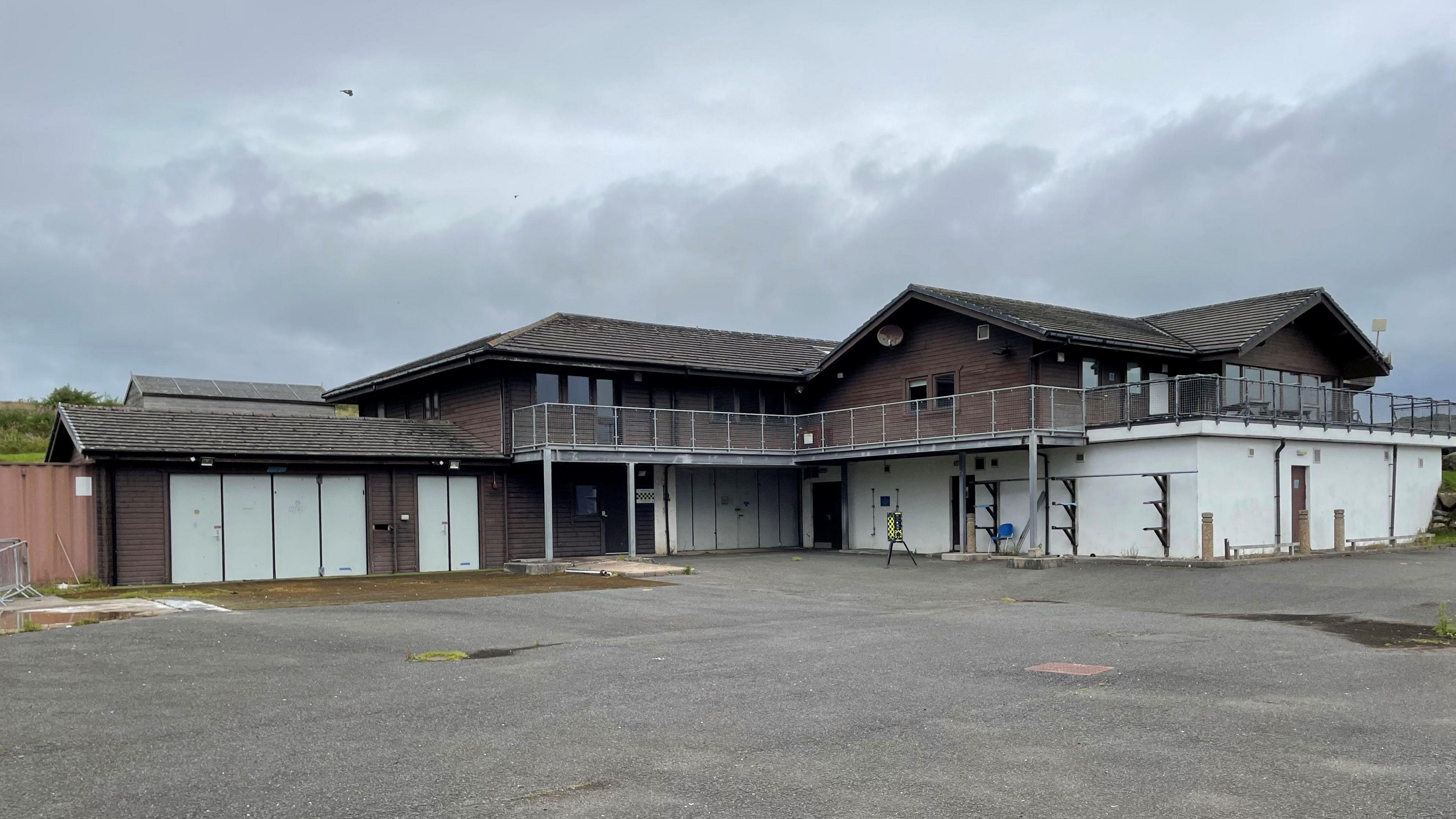 A disused building, previously used as a sports centre. Shutters are down around the building, and grey skies above it.