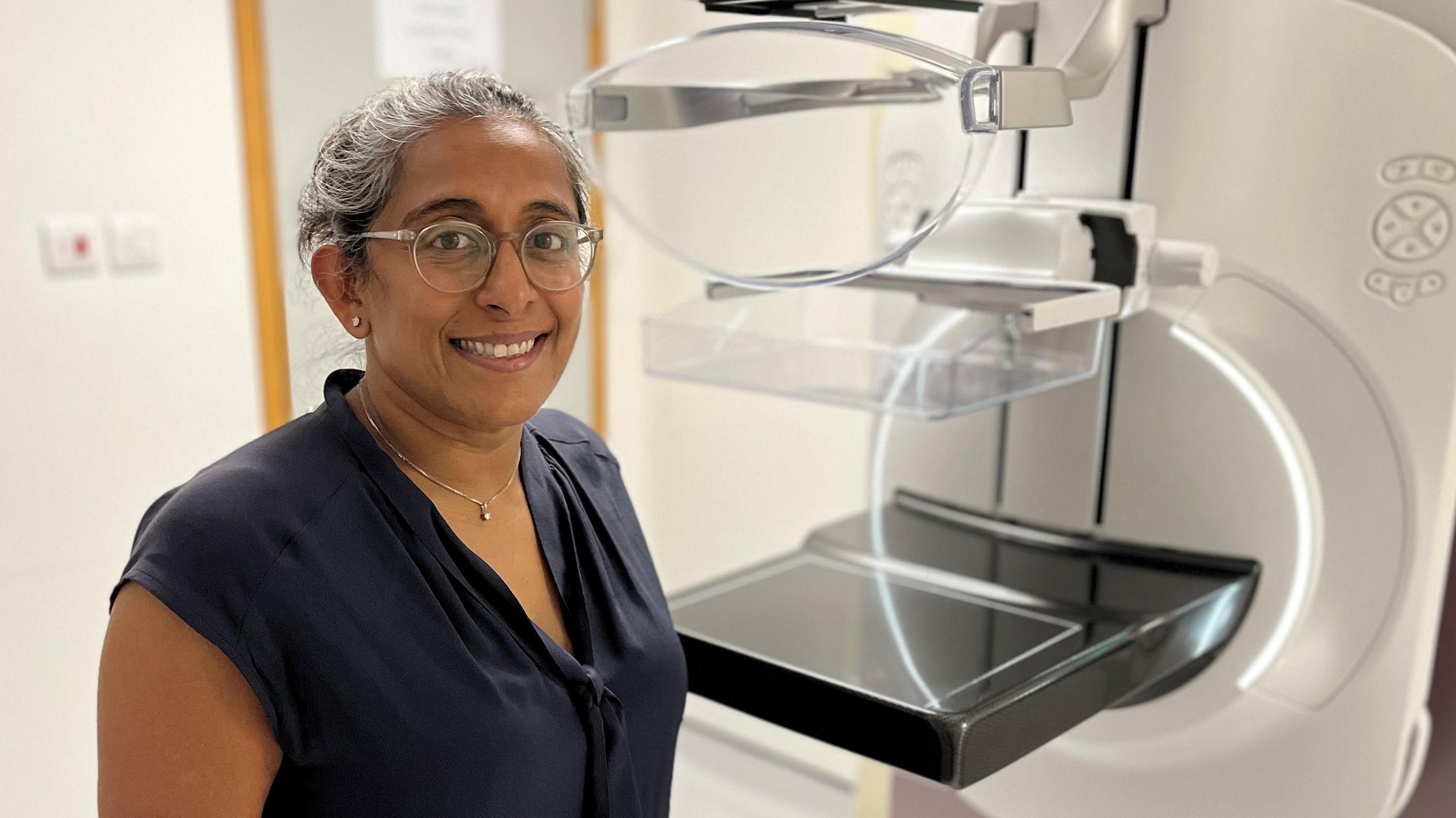 Dr Tamara Soaarist in a black top. She stands in front of a mammogram machine.