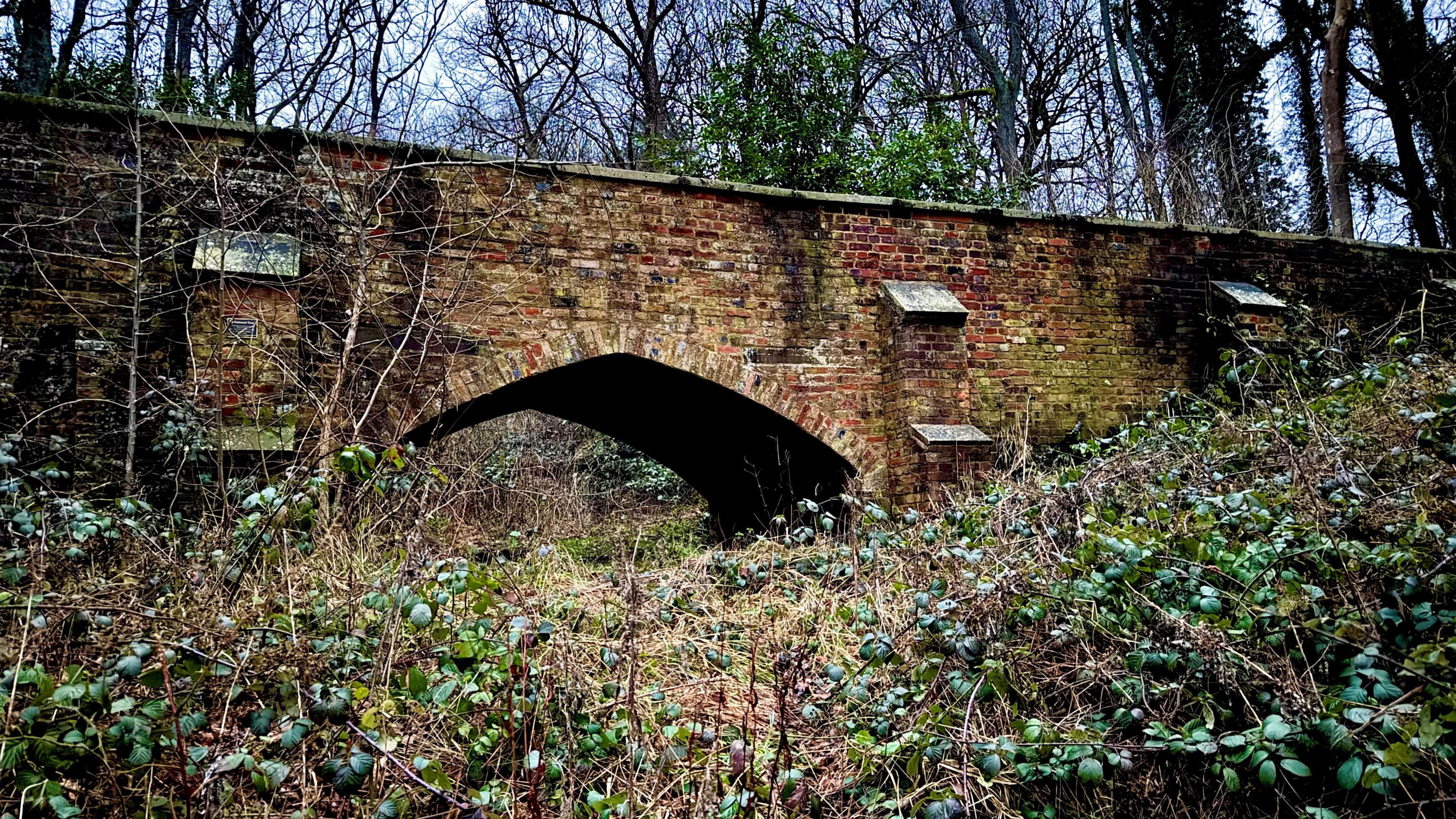 A large brick bridge, that has been repaired, showing bricks in place, and foliage all around it. 