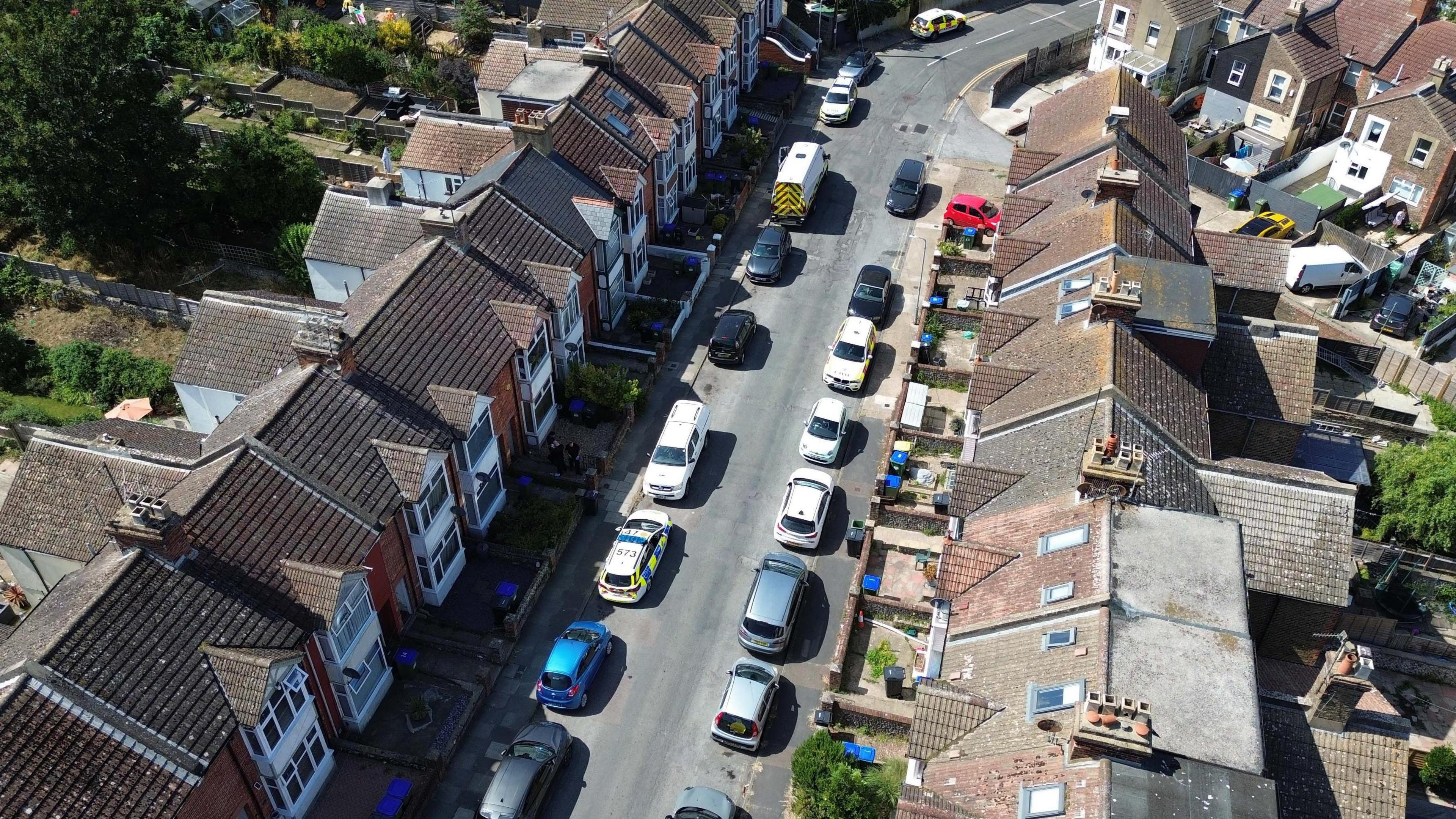 Two rows of terraces houses seen from above with vehicles, including police cars, parked on the street.