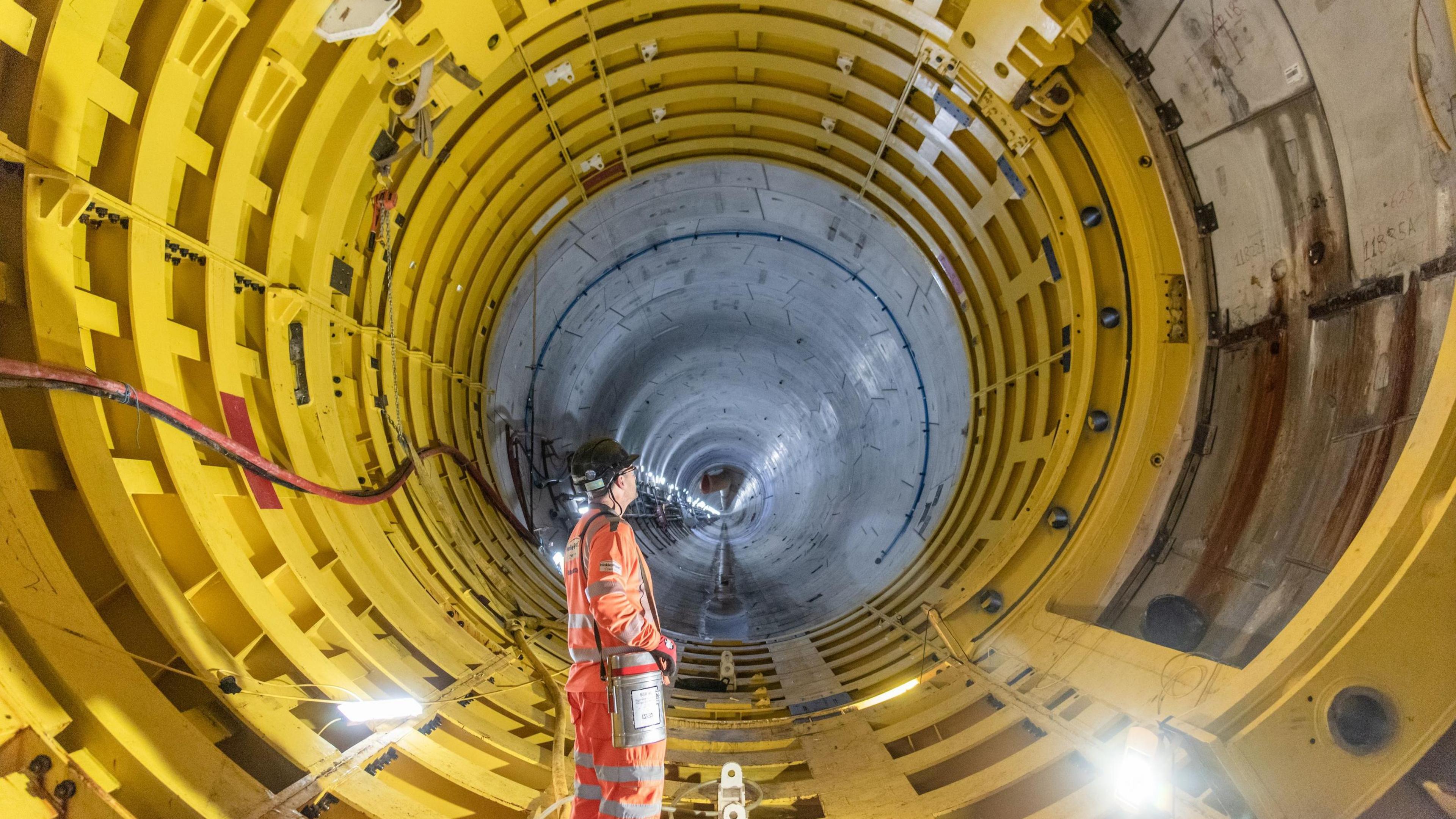 A worker stands in a six metre wide yellow tunnel which stretches away into the distance. It is one of several under the Bristol Channel at Hinkley Point C