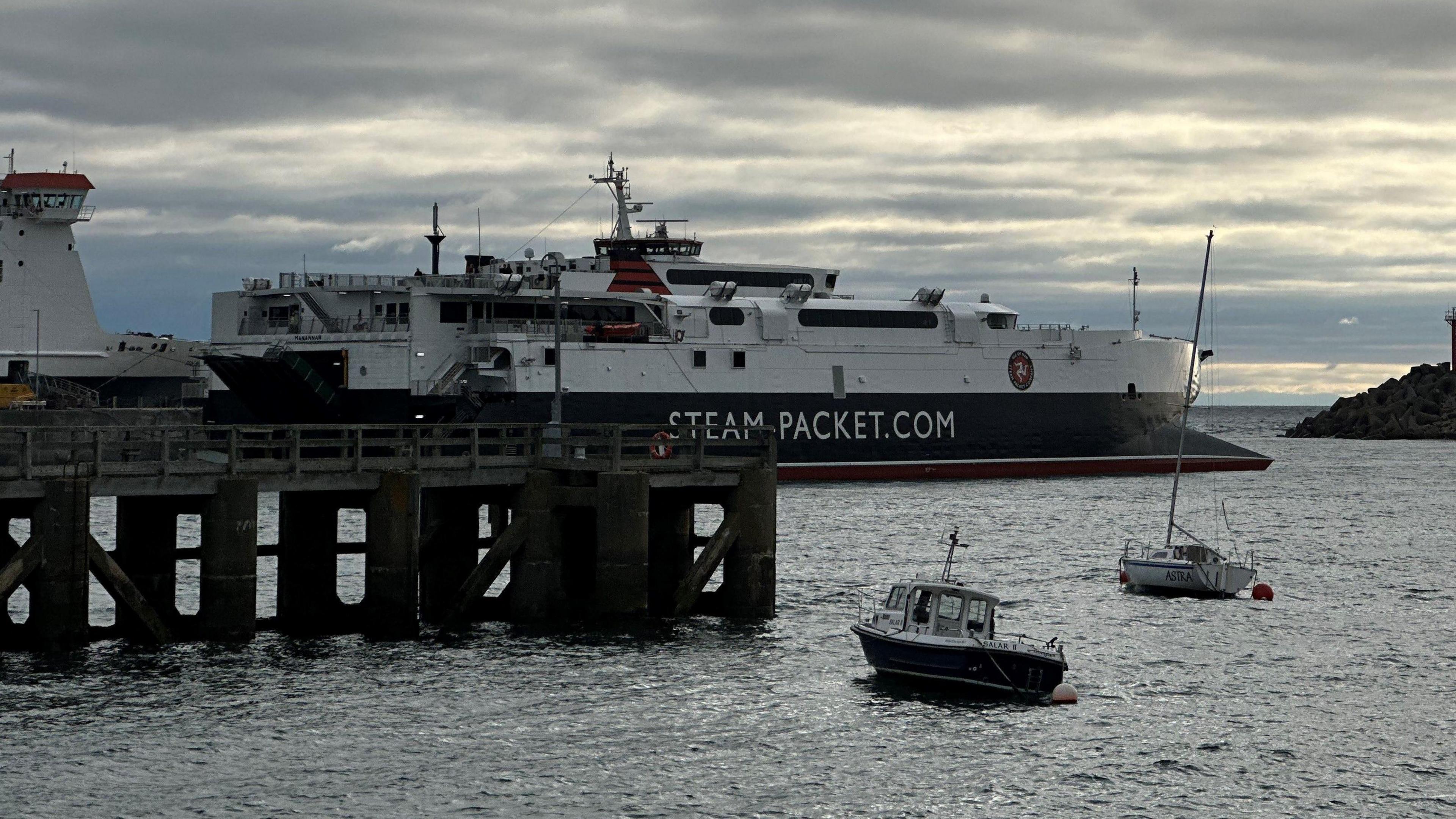 The Manannan, a sleek catamaran which is red, white and black and has Steam-Packet.com on the side in white lettering, as it leaves Douglas Harbour.