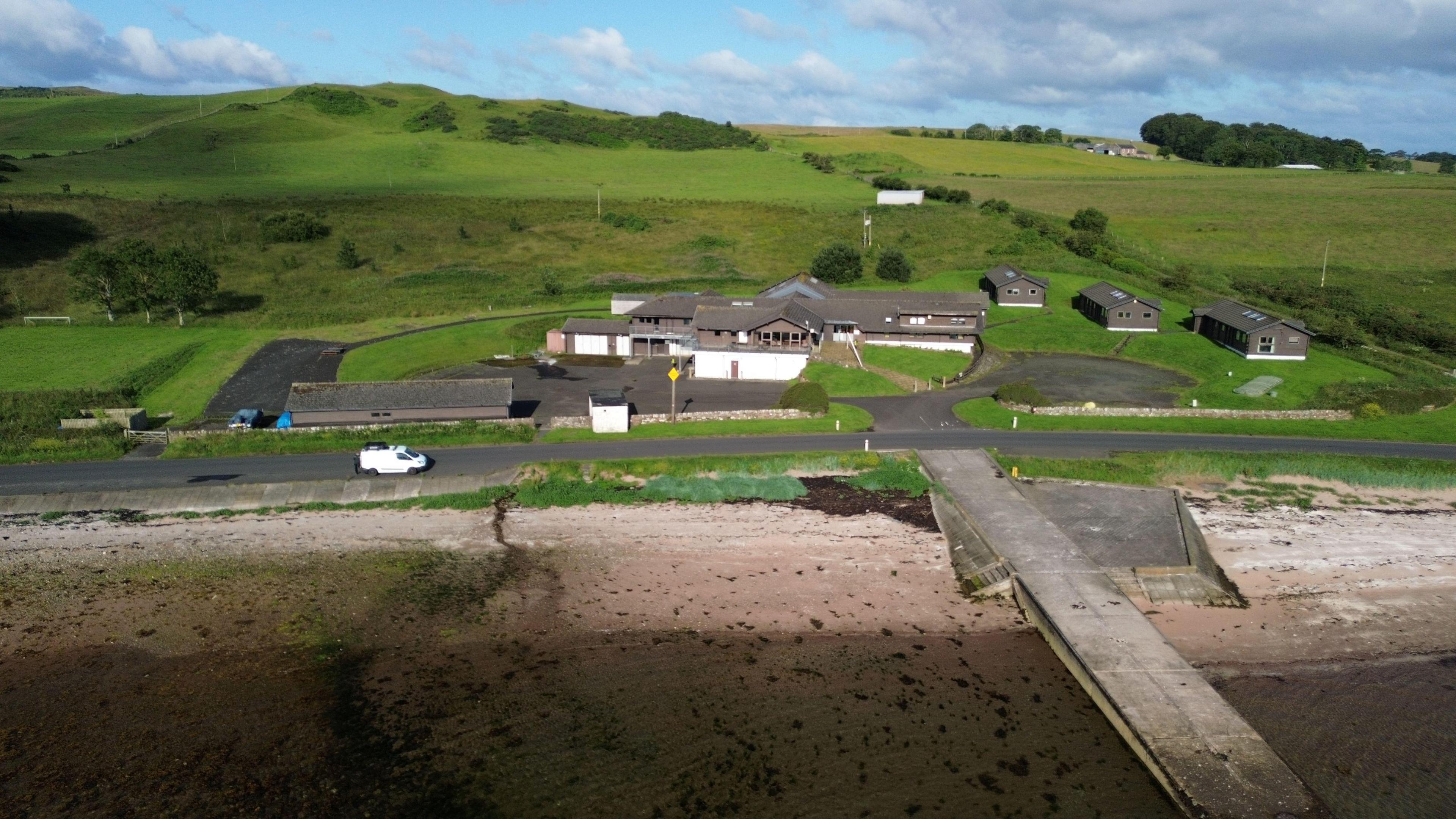 A view of the former national sports centre building from the sky. It is surrounded by greenspace, with a beach in front of it