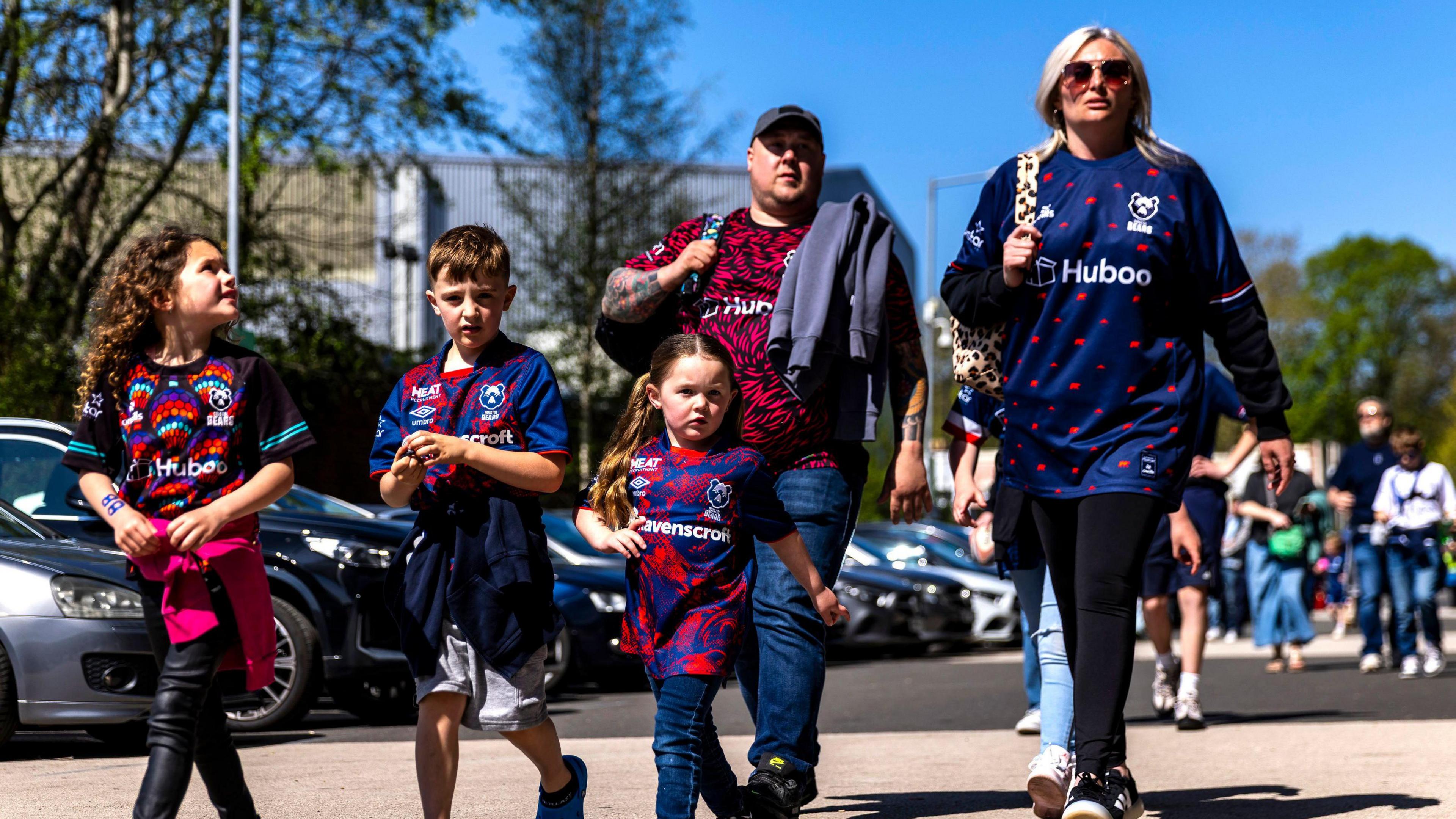 A family of Bristol Bears rugby fans walk towards Ashton Gate in the sunshine ahead of the match with the Leicester Tigers. The group is a man and a woman and three young children
