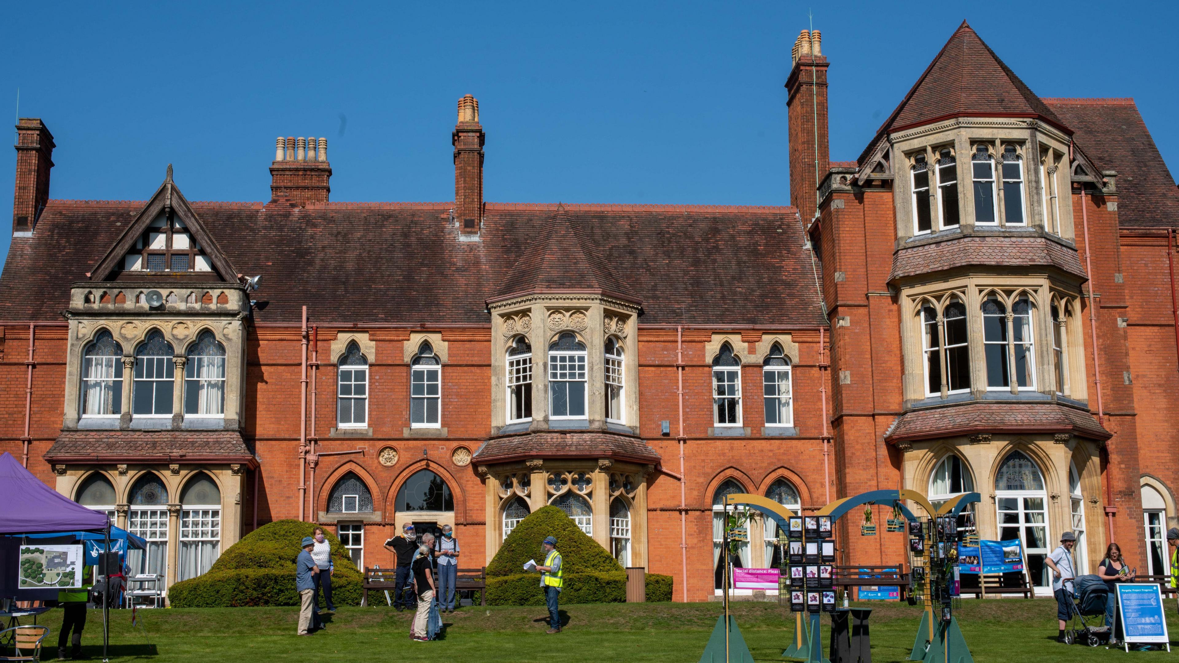 Highbury Hall, with its lawns in the foreground at what looks like an open day, with people looking at the front of the red brick building