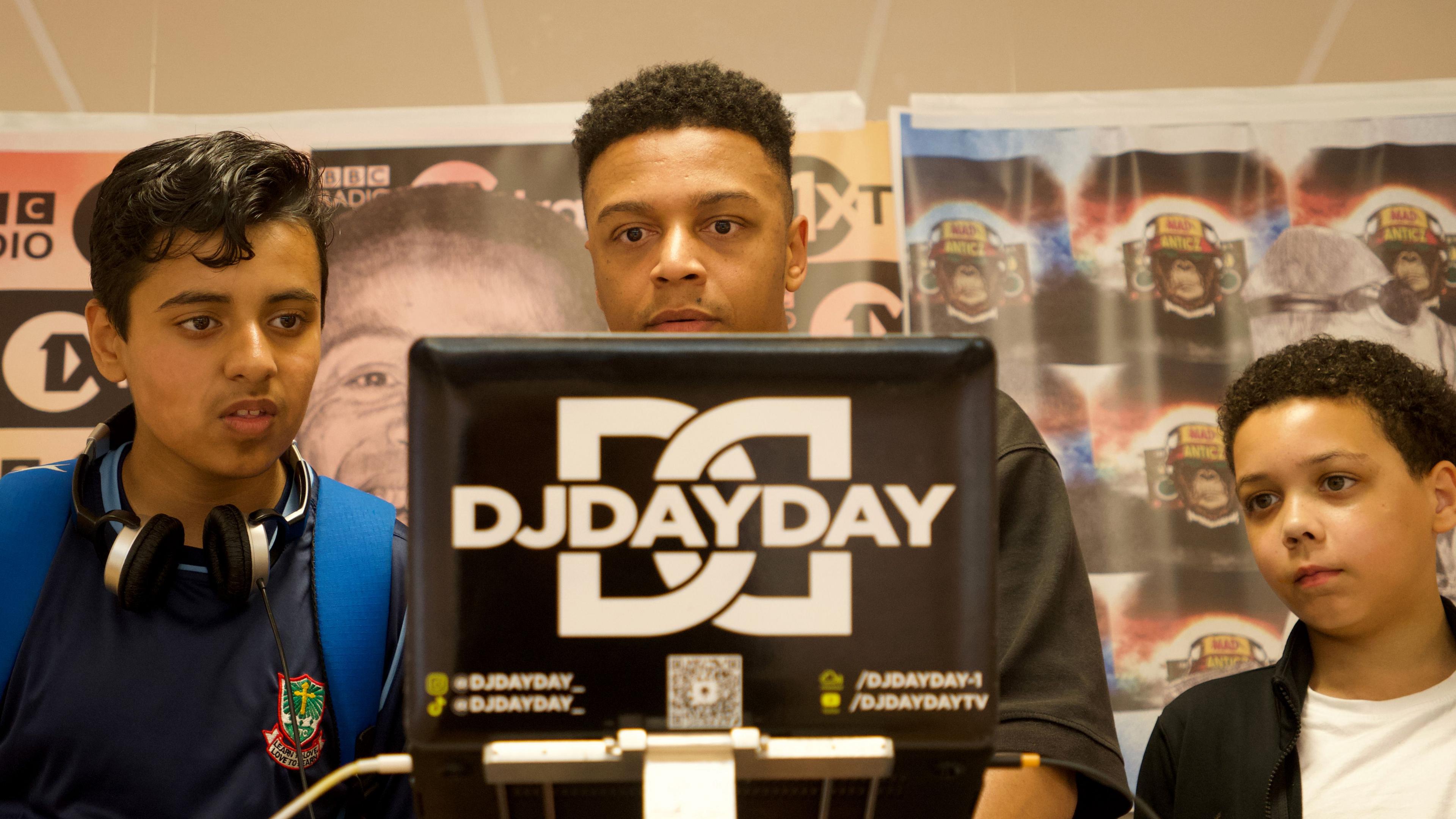 A man with short black hair looking at a laptop screen flanked by two teenage boys.