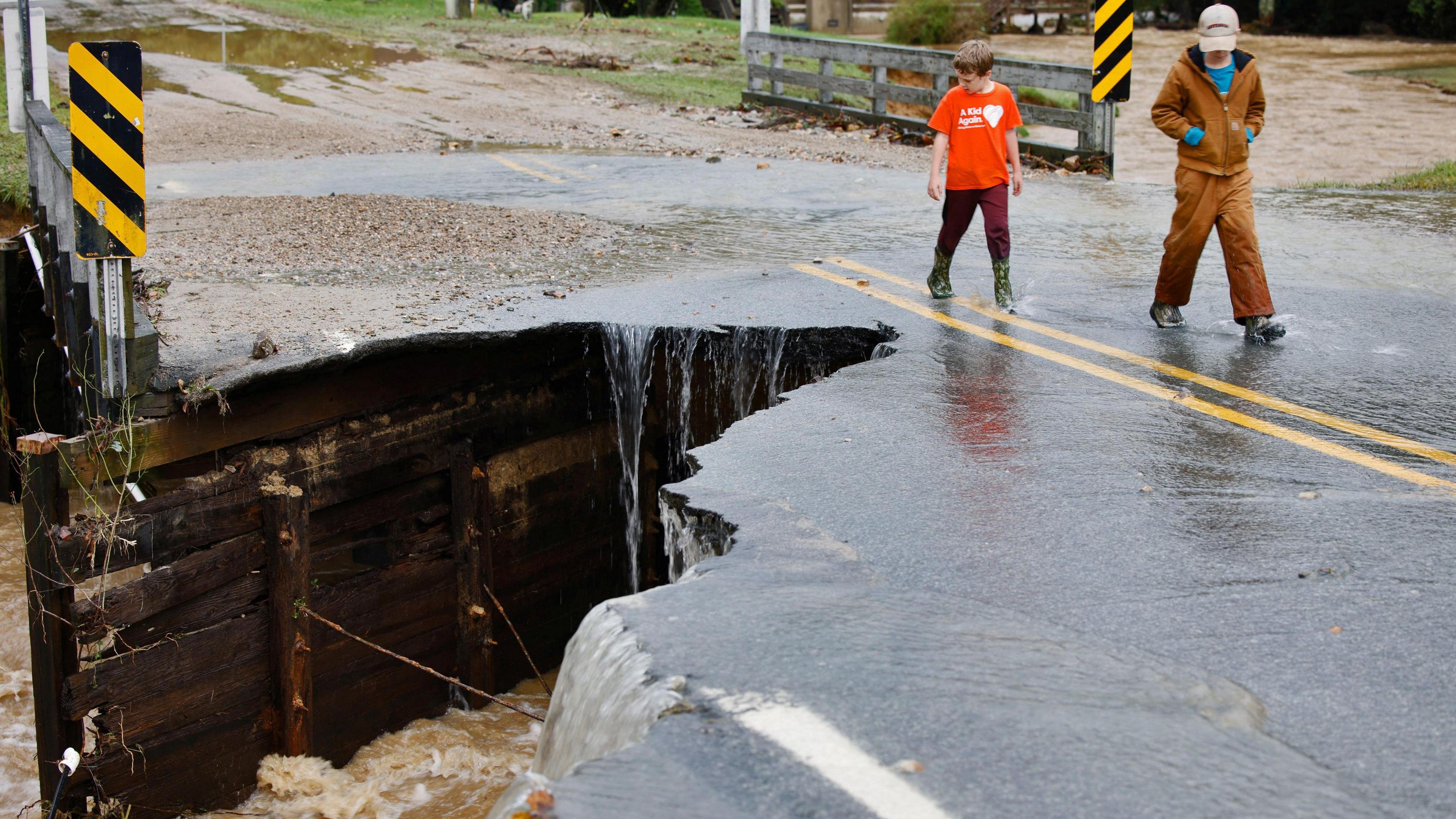 Children walk past the collapsed portion of a bridge after flood waters destroyed it, in Boone, North Carolina