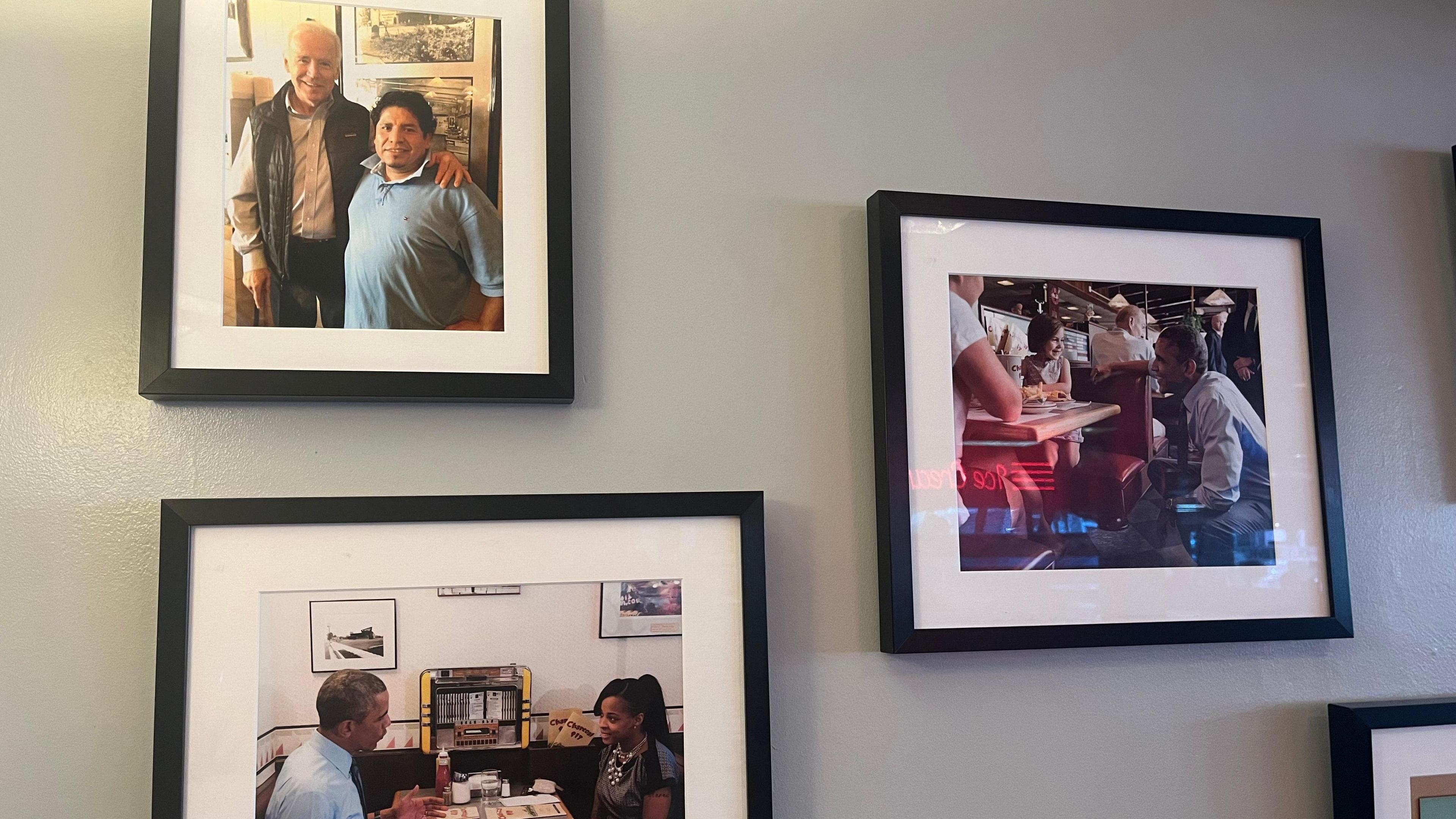 On a grey wall there are three images in a black frame. One is of Biden at the diner and the other two are of Barack Obama sitting and kneeling next to a diner table speaking to customers.