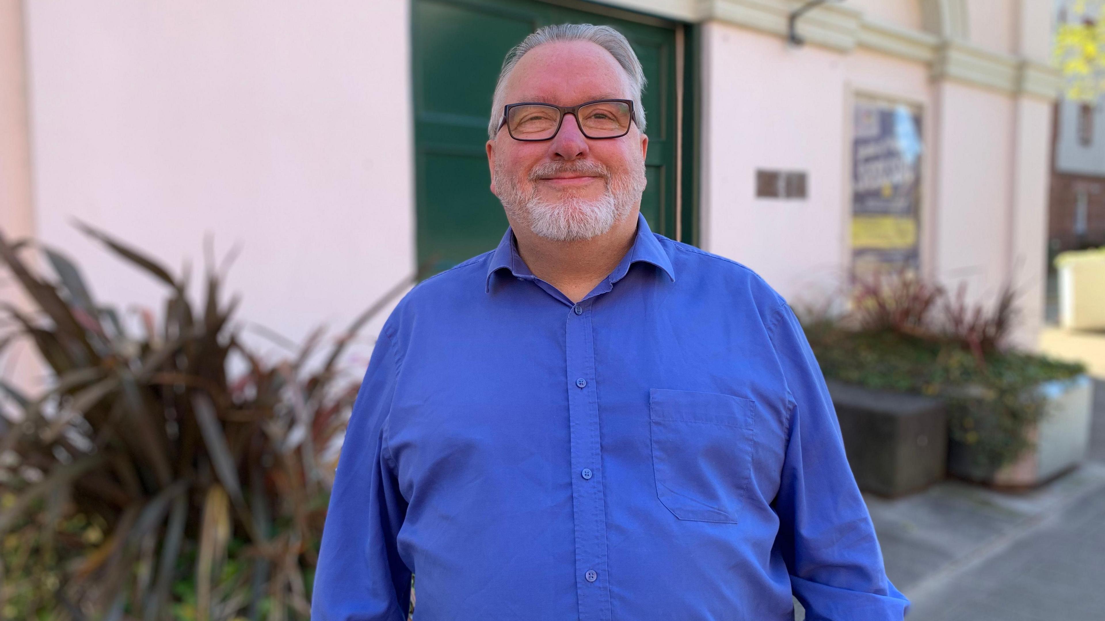 A man standing outside the theatre smiling with a blue shirt on.