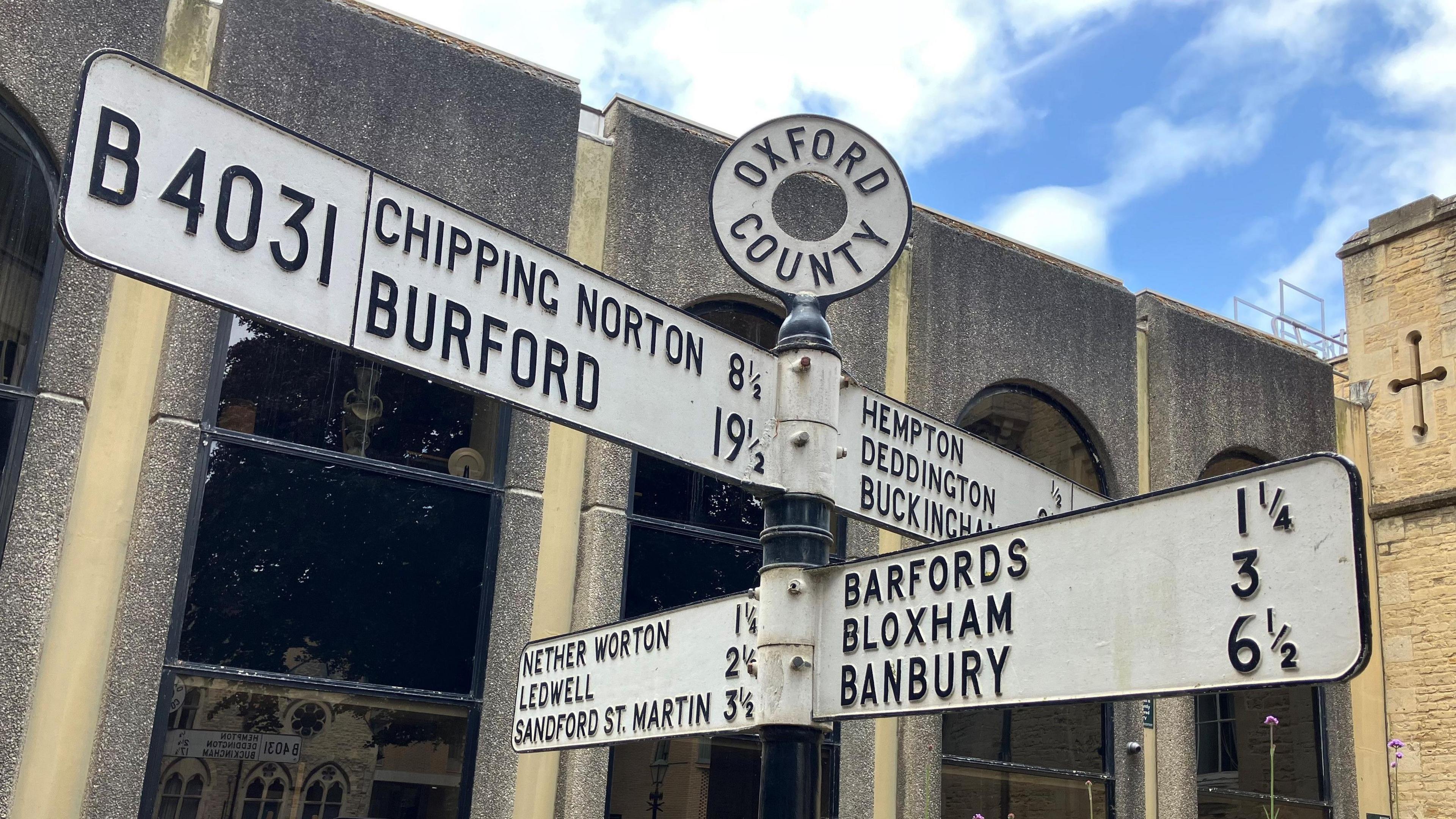 An old-style road sign outside County Hall in Oxford shows the direction and distances to a number of different places in and around Oxfordshire.