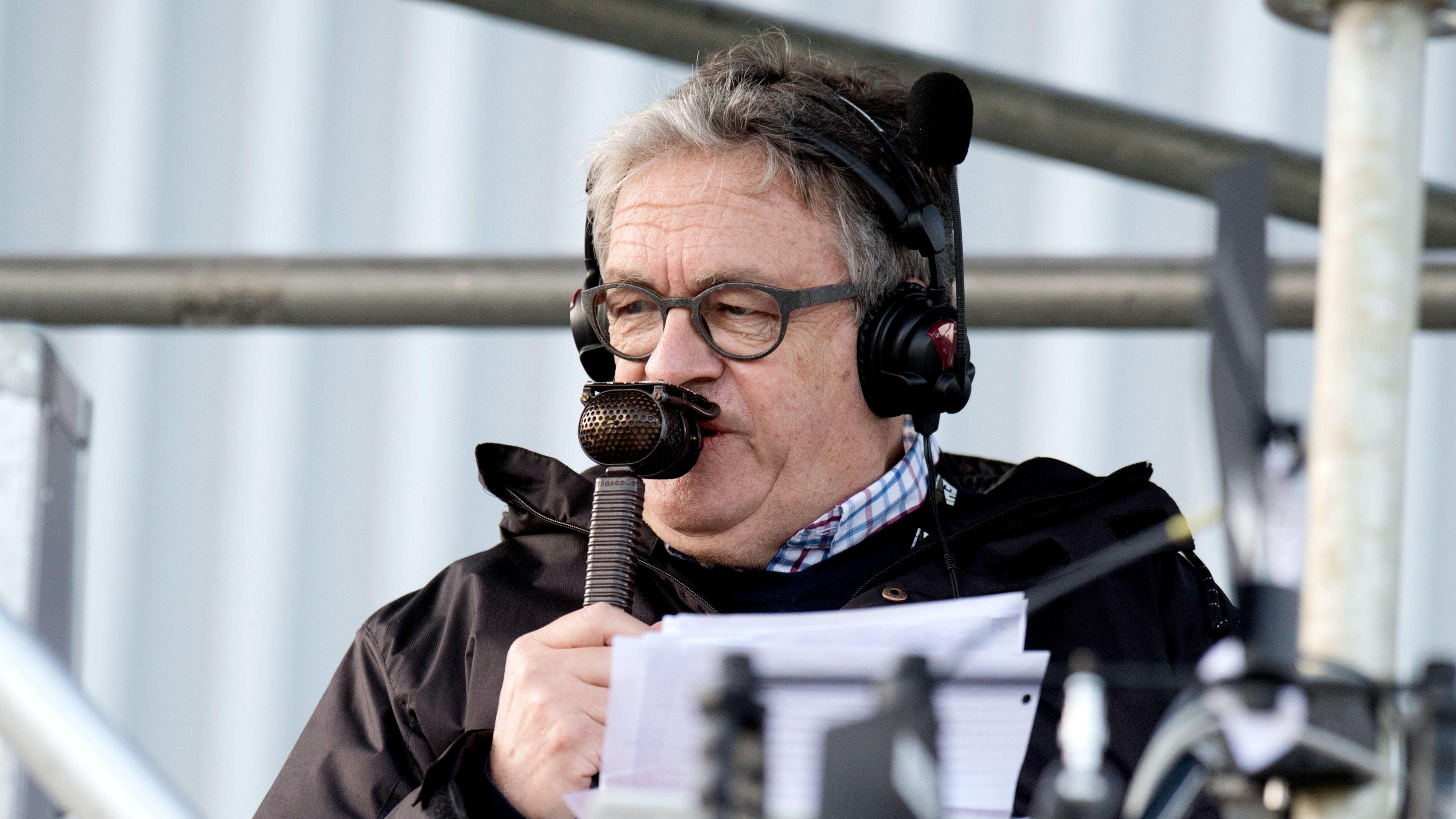 Nick Irvine commentating during a game. He has headphones on and is speaking into a microphone. He is also holding sheets of paper. 