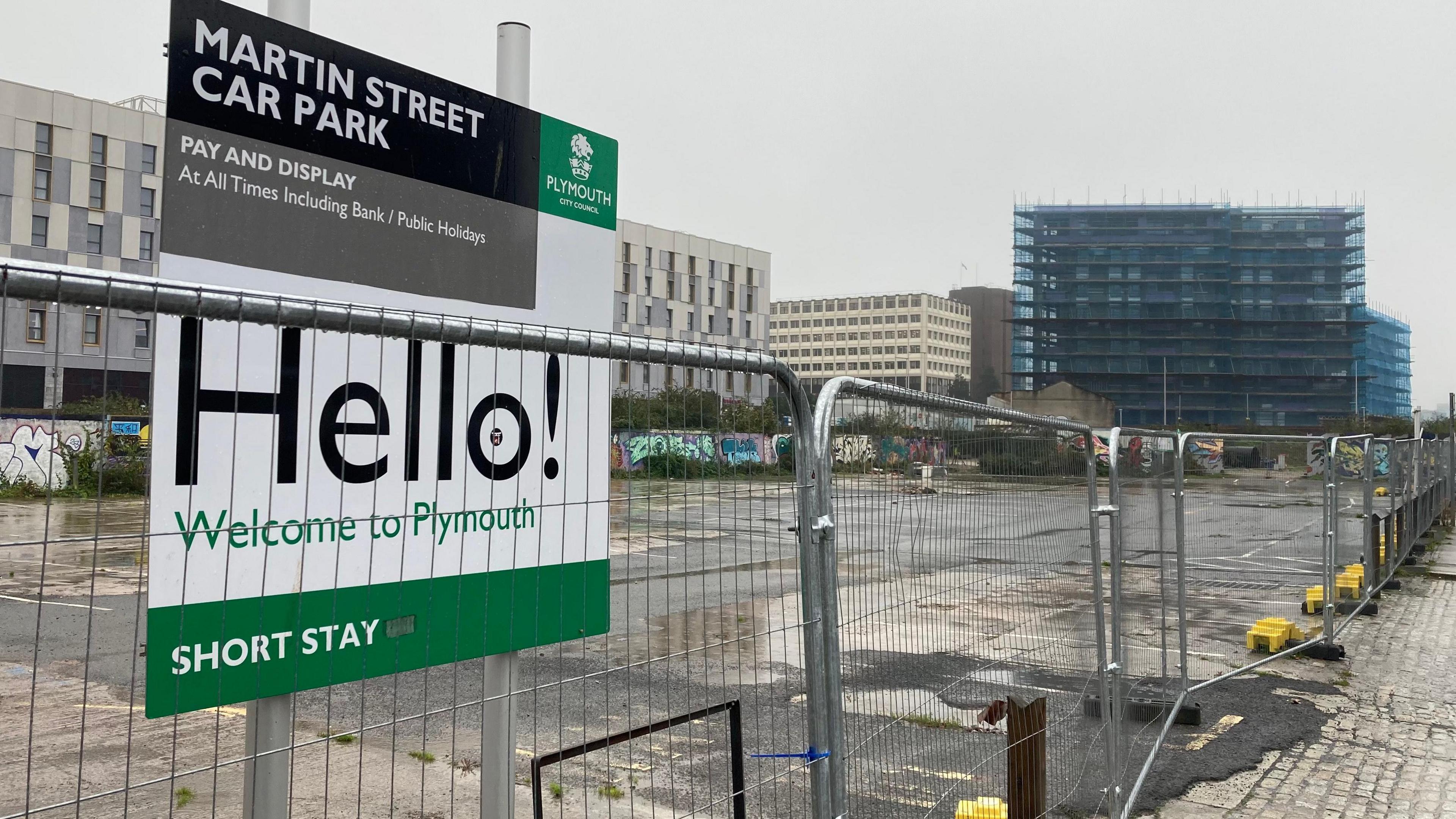 A building site on Martin Street in Plymouth which has fencing up around it and a sign for a former car park with the words "hello, welcome to Plymouth" written on it.