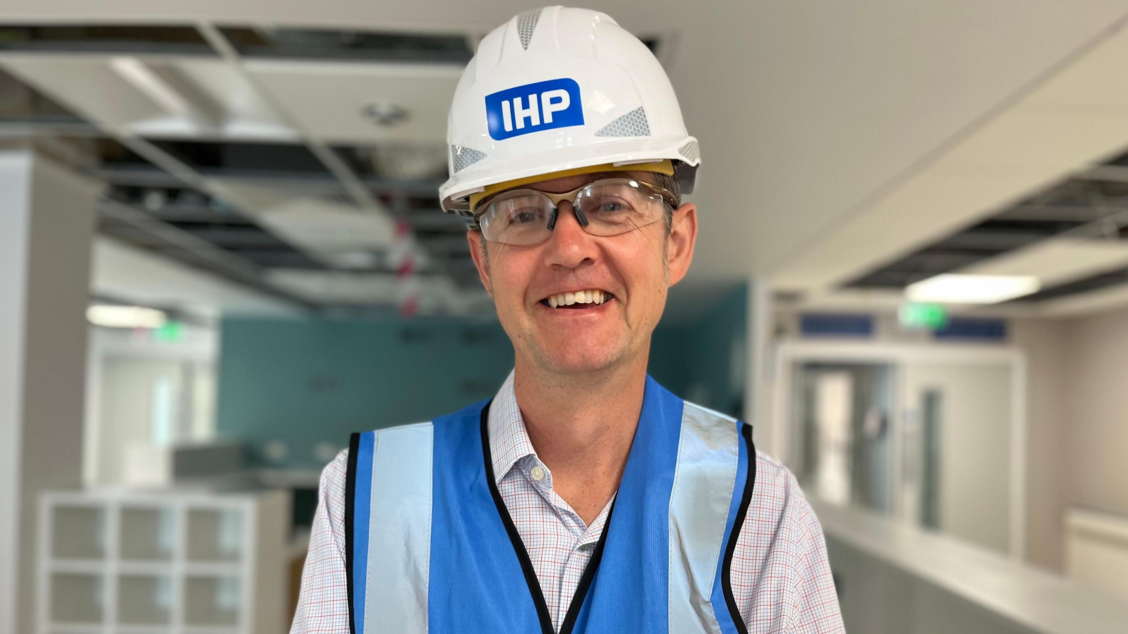 Dr Ed Smith wearing a hard hat and a blue high visibility jacket standing in an empty hospital ward