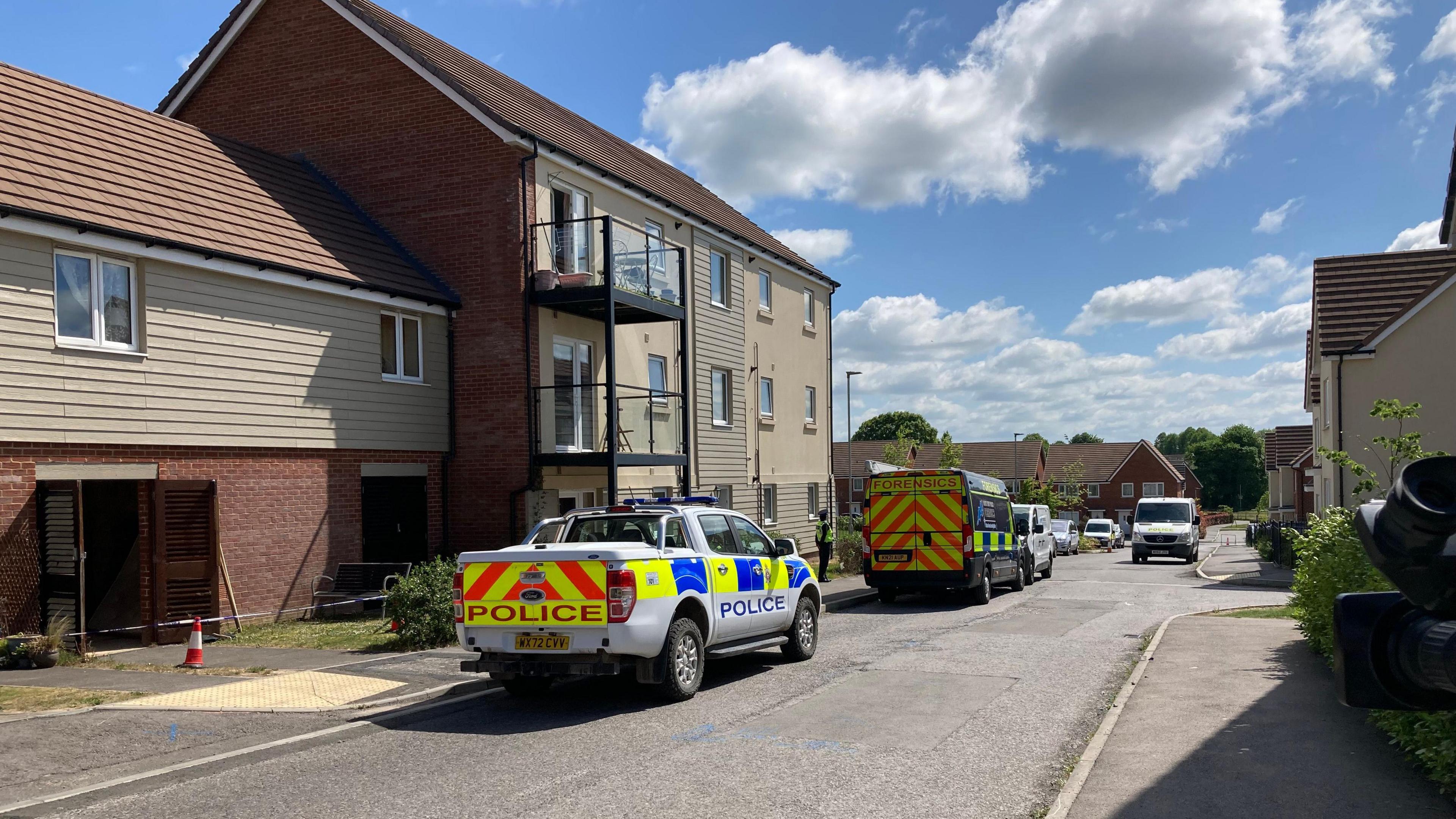 A police car and police forensics van parked outside some houses on Davies Road in Salisbury. Police tape surrounds one of the properties.