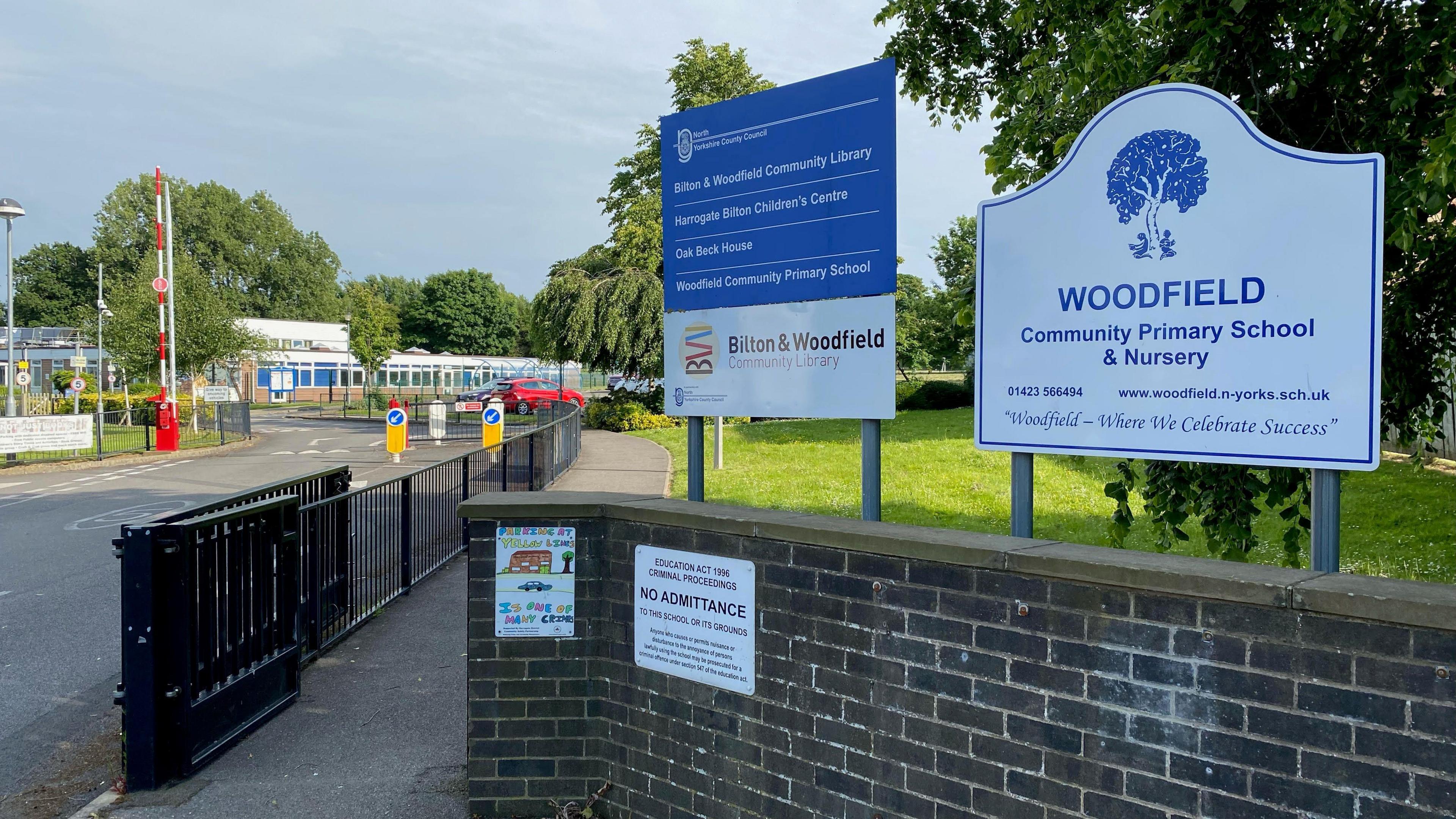 The entrance to a primary school car park, as indicated by a sign saying 'Woodfield Community Primary School & Nursery'.