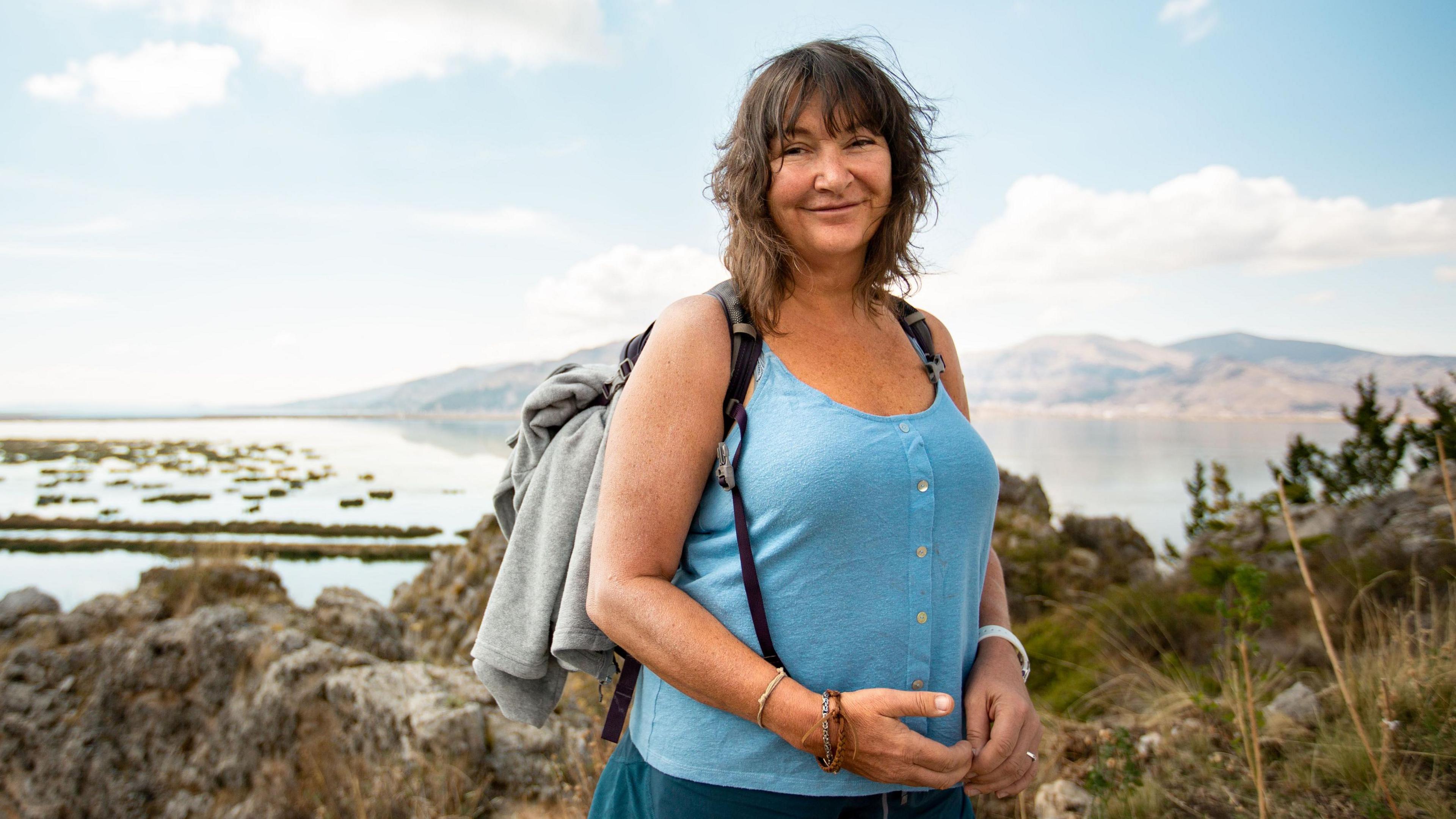 Woman in blue vest and shorts wearing a grey rucksack
