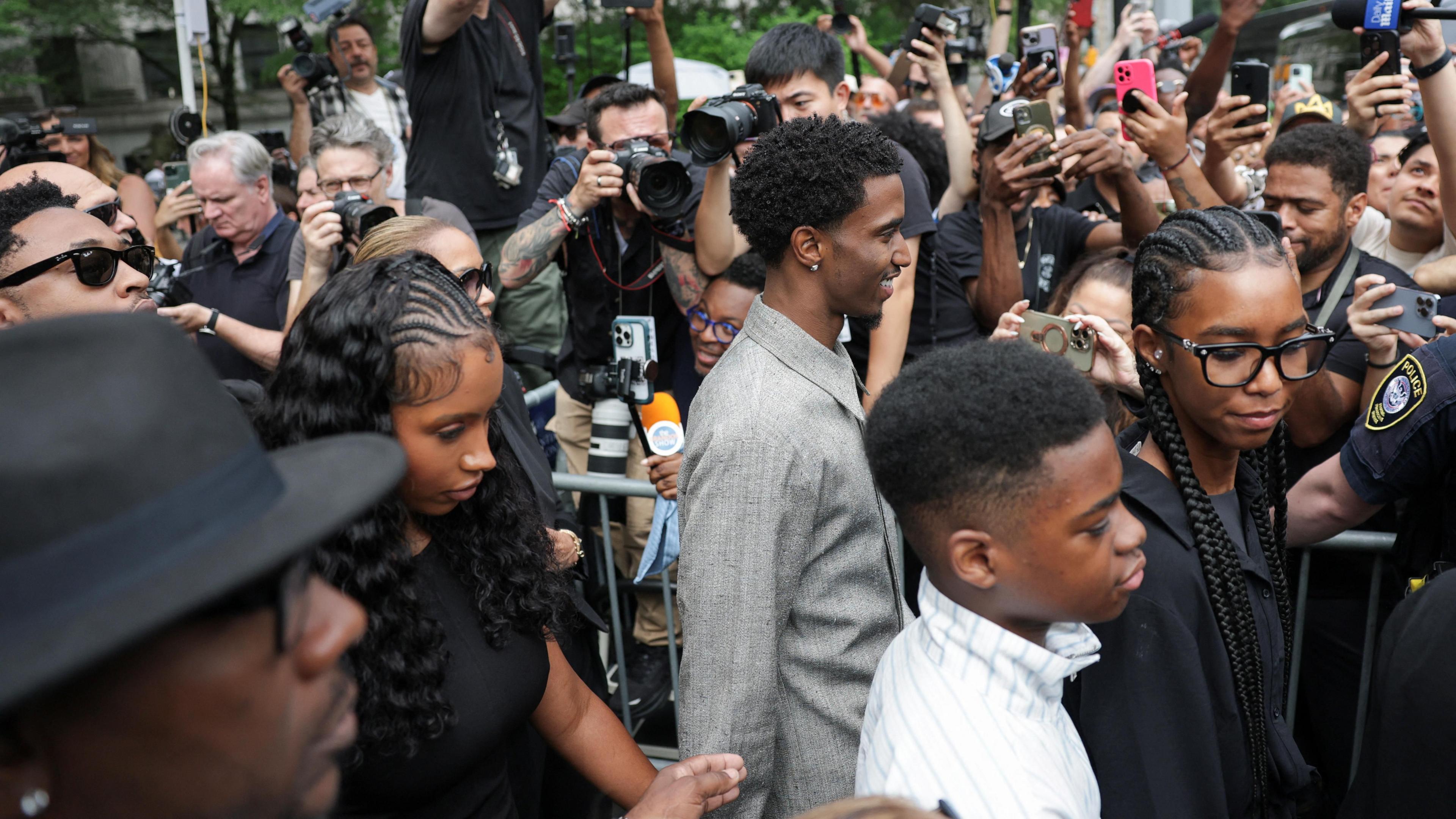 Three people walk through a crowd of cameras 
