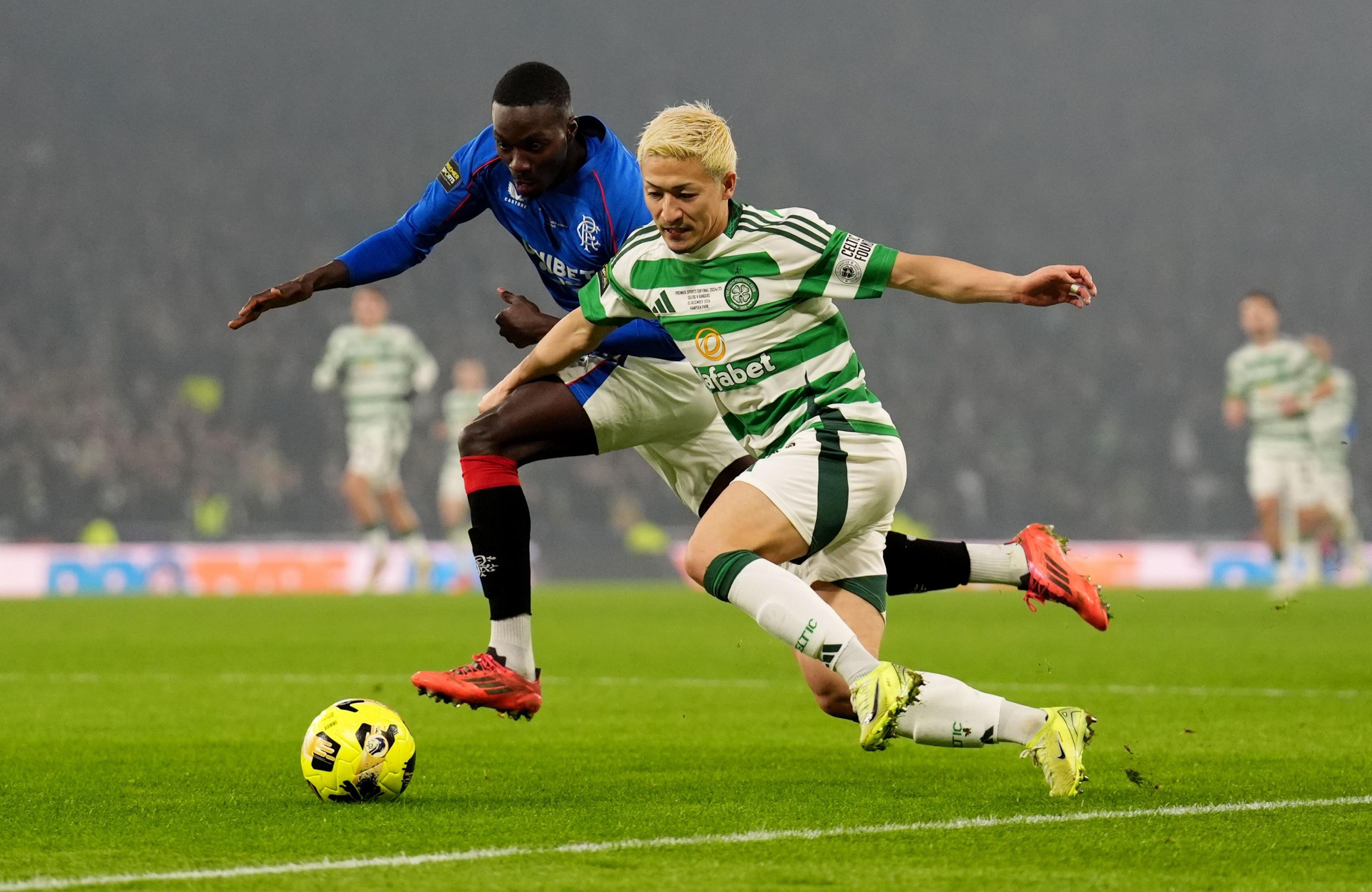 Celtic player Daizen Maeda, who is wearing a green and white hooped football tope, white an green shorts, white and green socks and yellow boots battles for the ball with Rangers midfielder Mohammed Diomande who is wearing a blue top, white and blue shorts, red, black and white socks and pink boots at Hampden Park