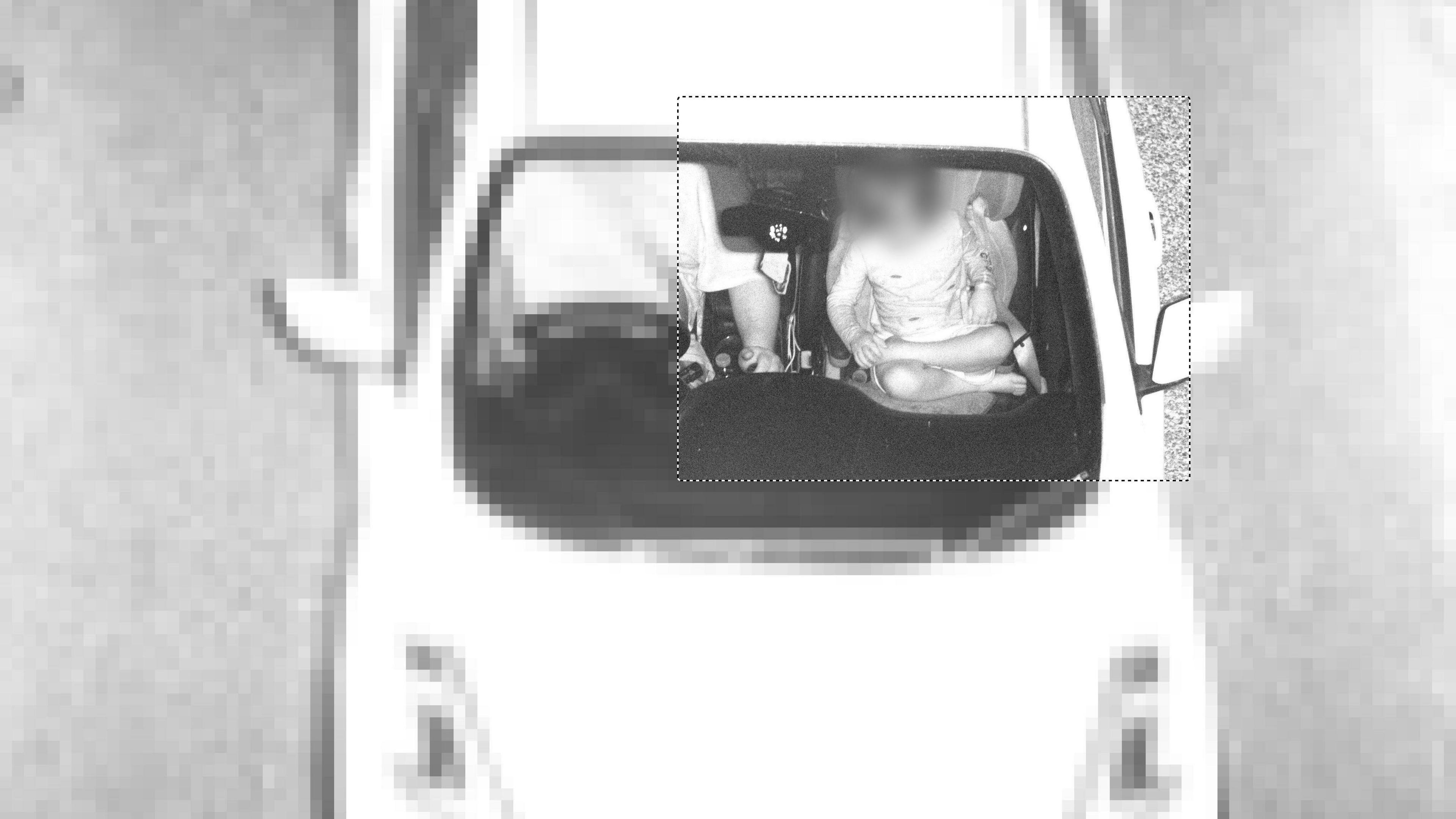 A child sits cross-legged in the front passenger seat of a car with no seatbelt while the adult driving wears a seatbelt