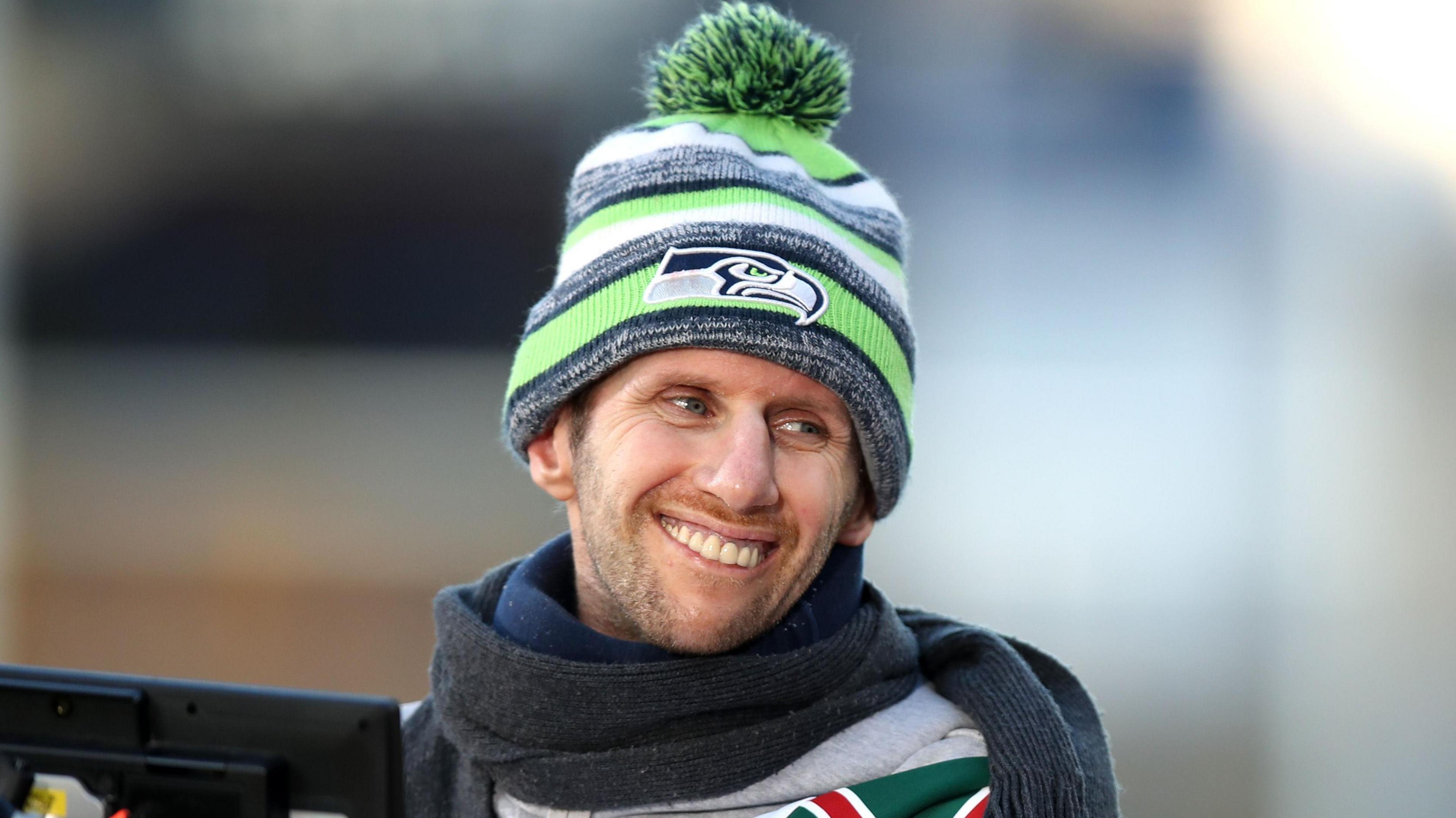 Rob Burrow smiling at someone to the side of him. He is wearing a green, black and white striped bobble hat.