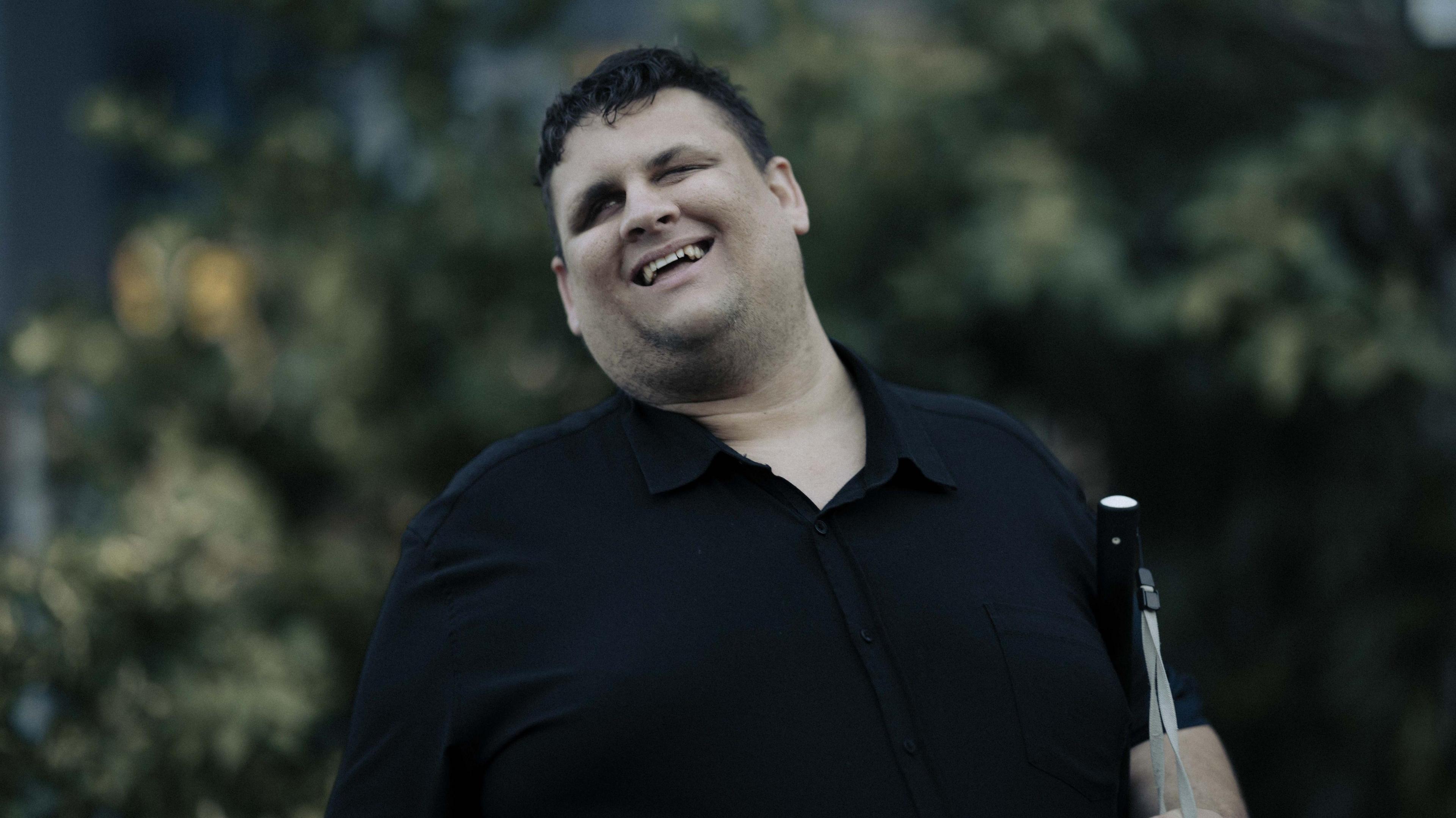A man wearing a black shirt, carrying a white cane