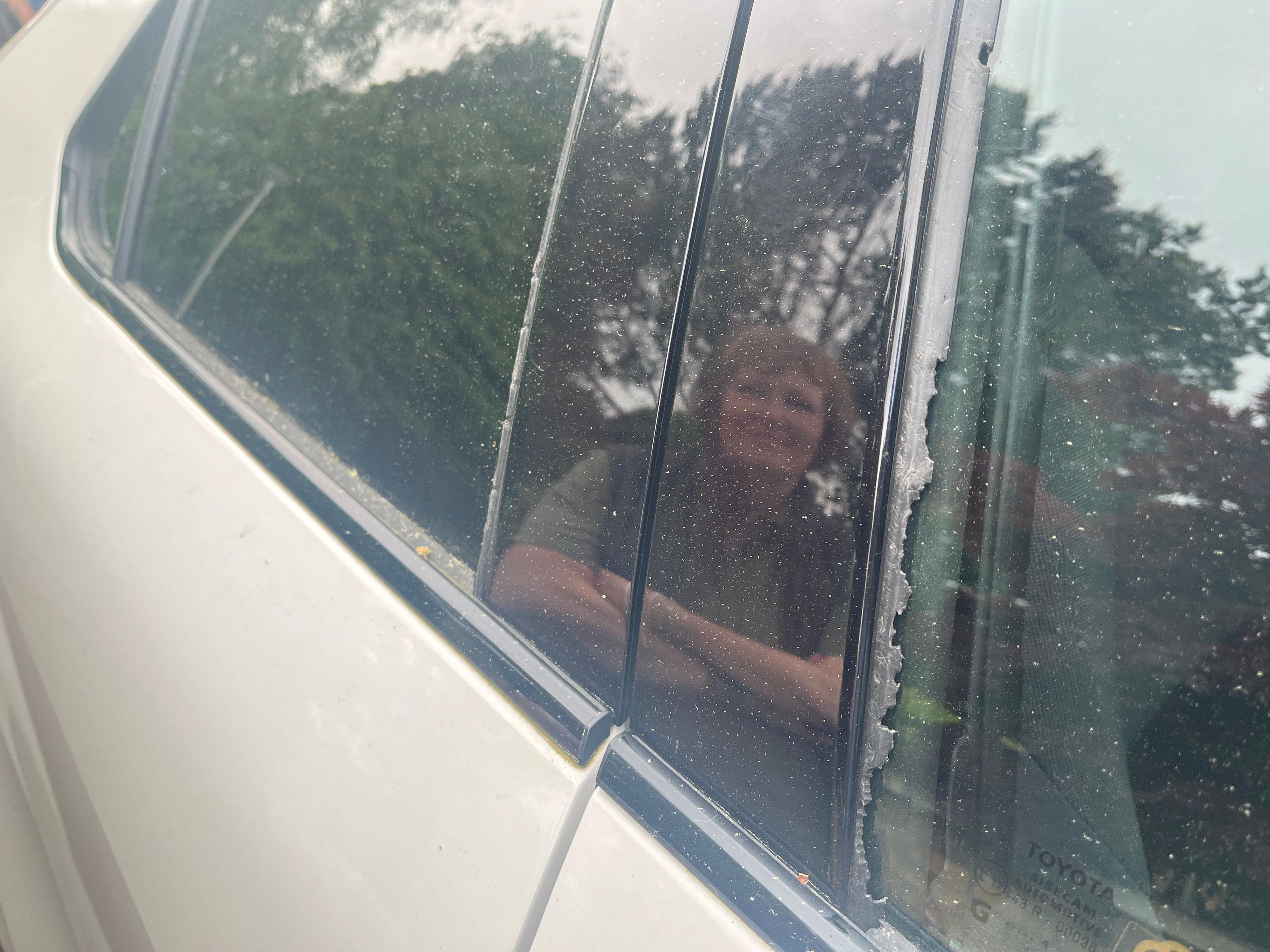 A photograph of the damaged car window seal. The reflection of a woman is visiable in the door frame. 