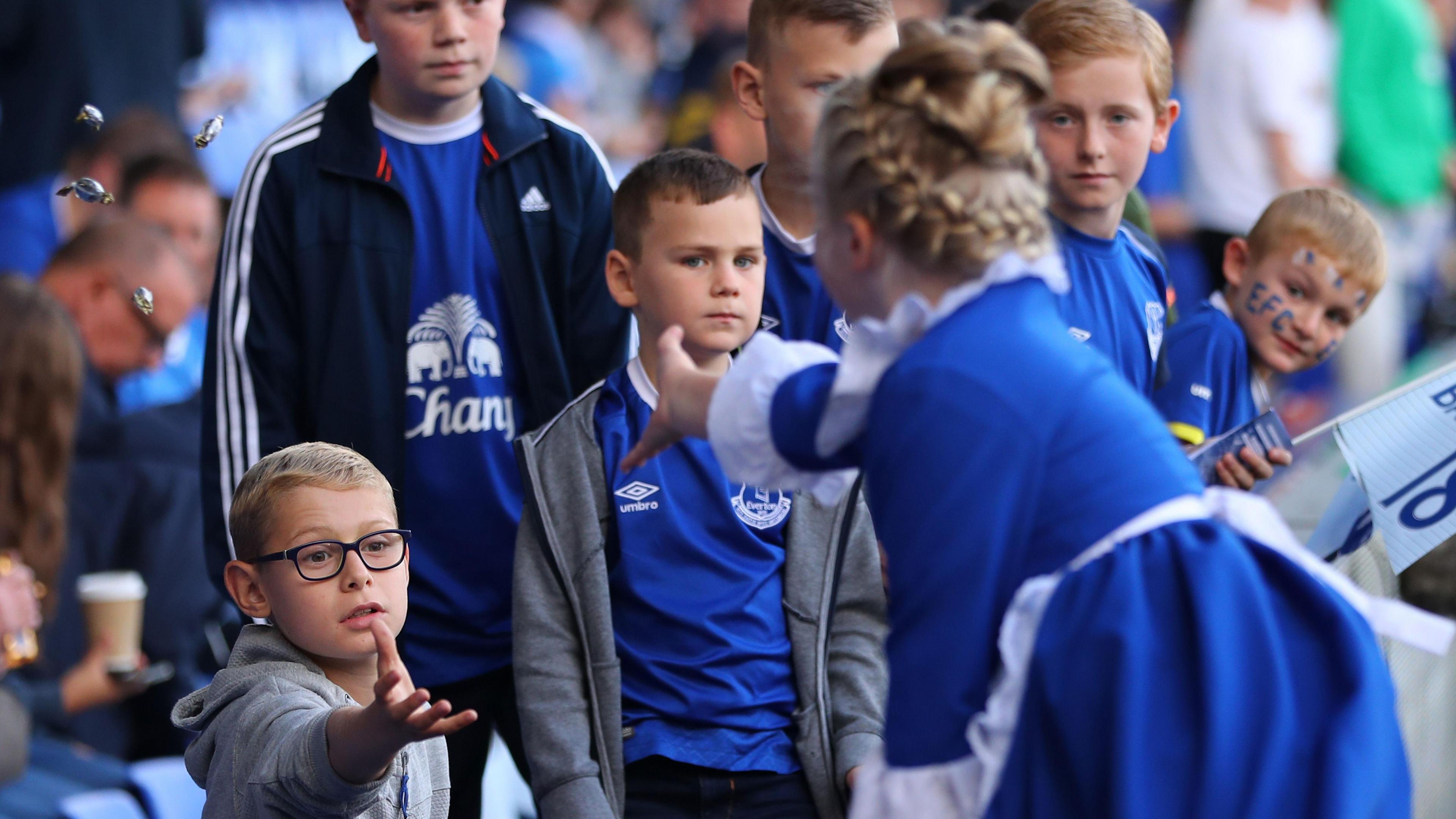 An Everton toffee lady, wearing a traditional blue dress and white pinny, gives out sweets to young Everton fans at Goodison Park.