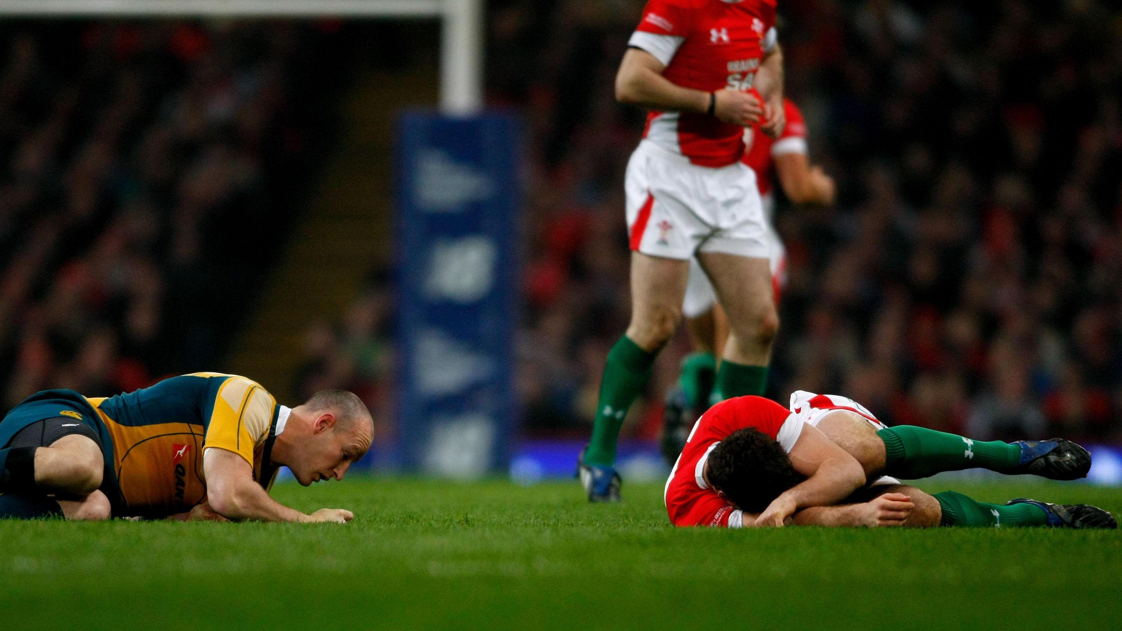Jamie Roberts lies injured on a rugby pitch while wearing the red of Wales. Australian captain Stirling Mortlock lies on the grass to Jamie's left. 