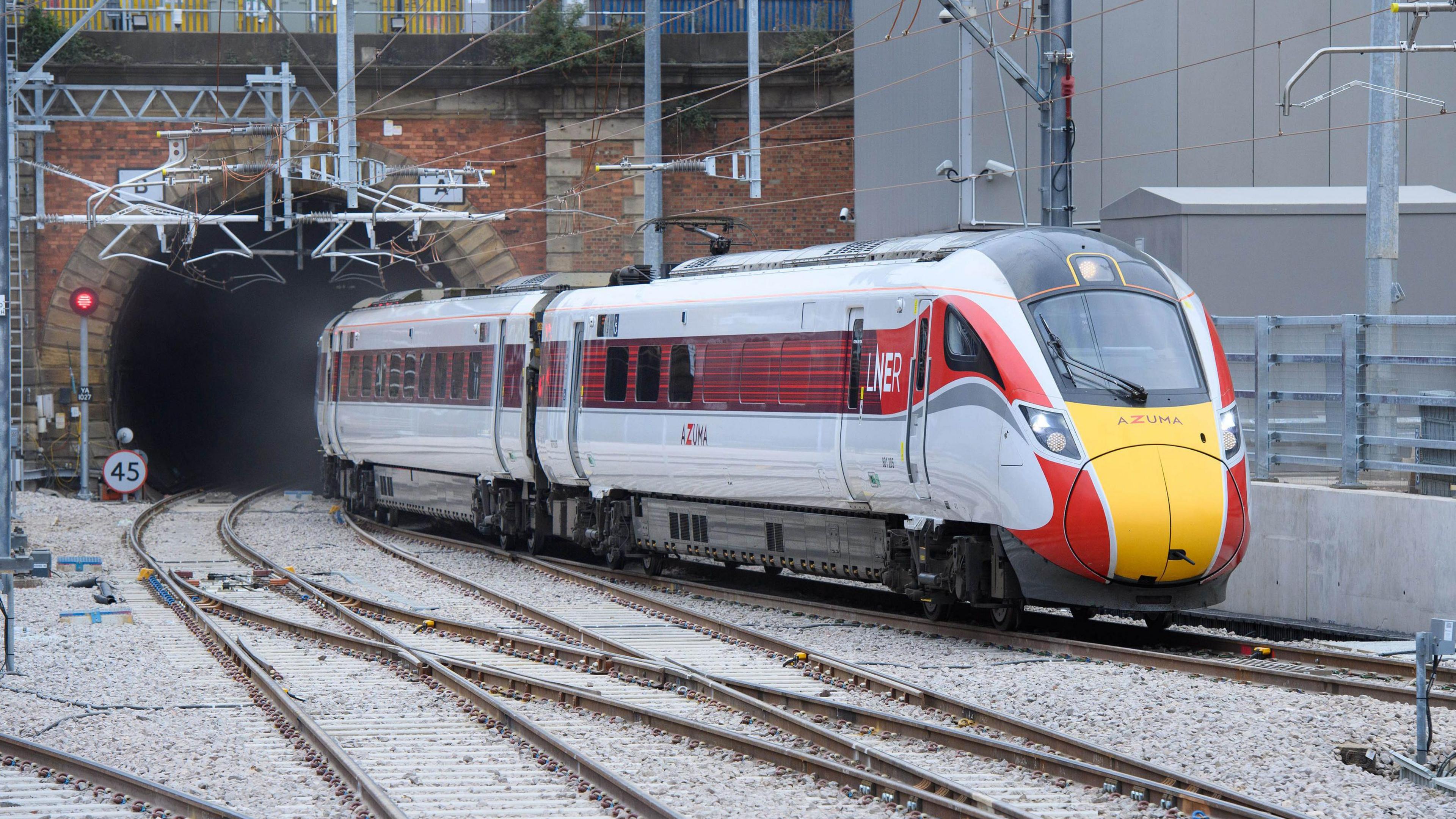 An LNER Azuma train heading into King's Cross Station. The red, grey and yellow train is leaving a tunnel and is nearing the station.