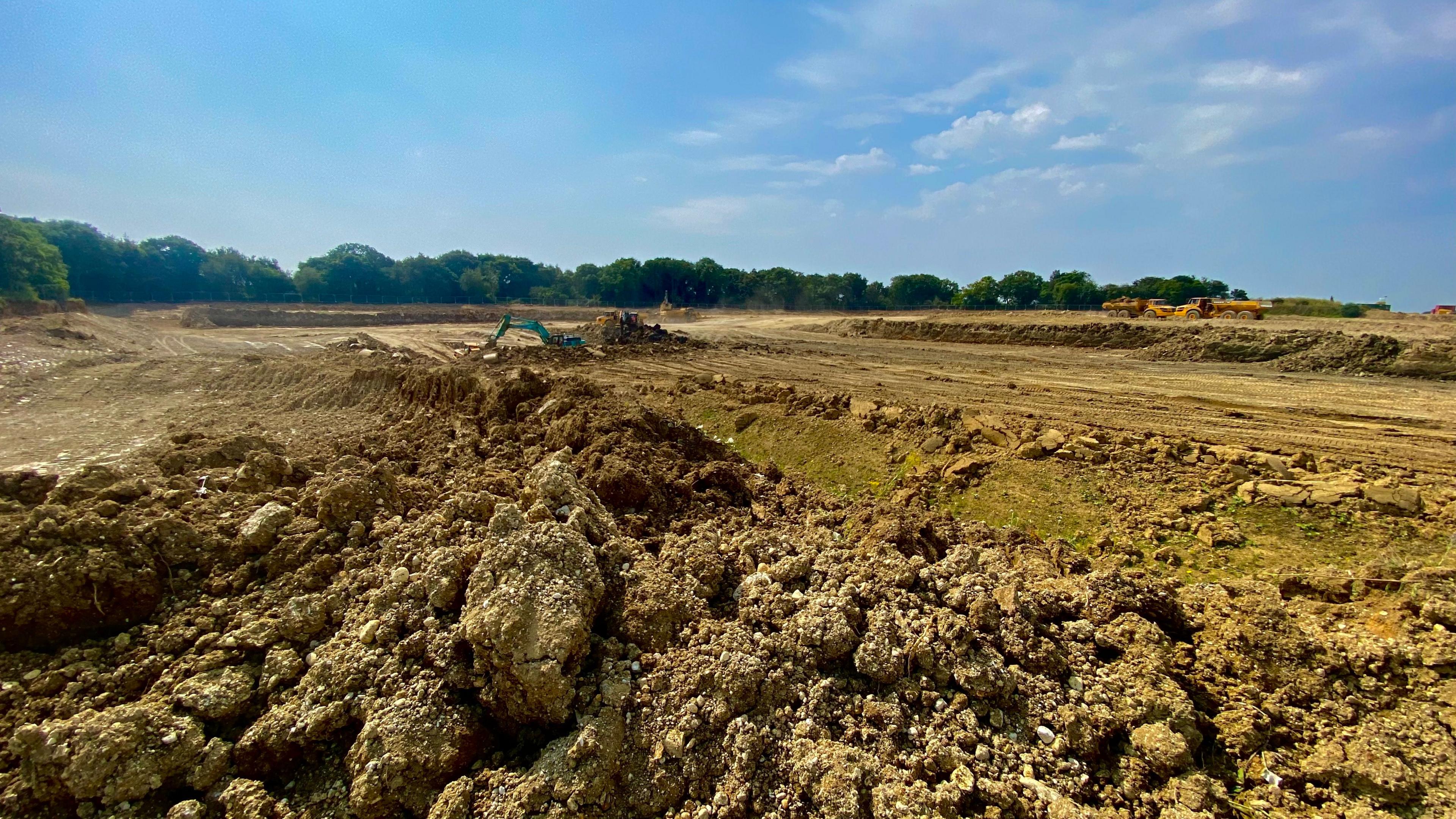 A landscape of mud being dug up by a blue digger, which is visible in the distance