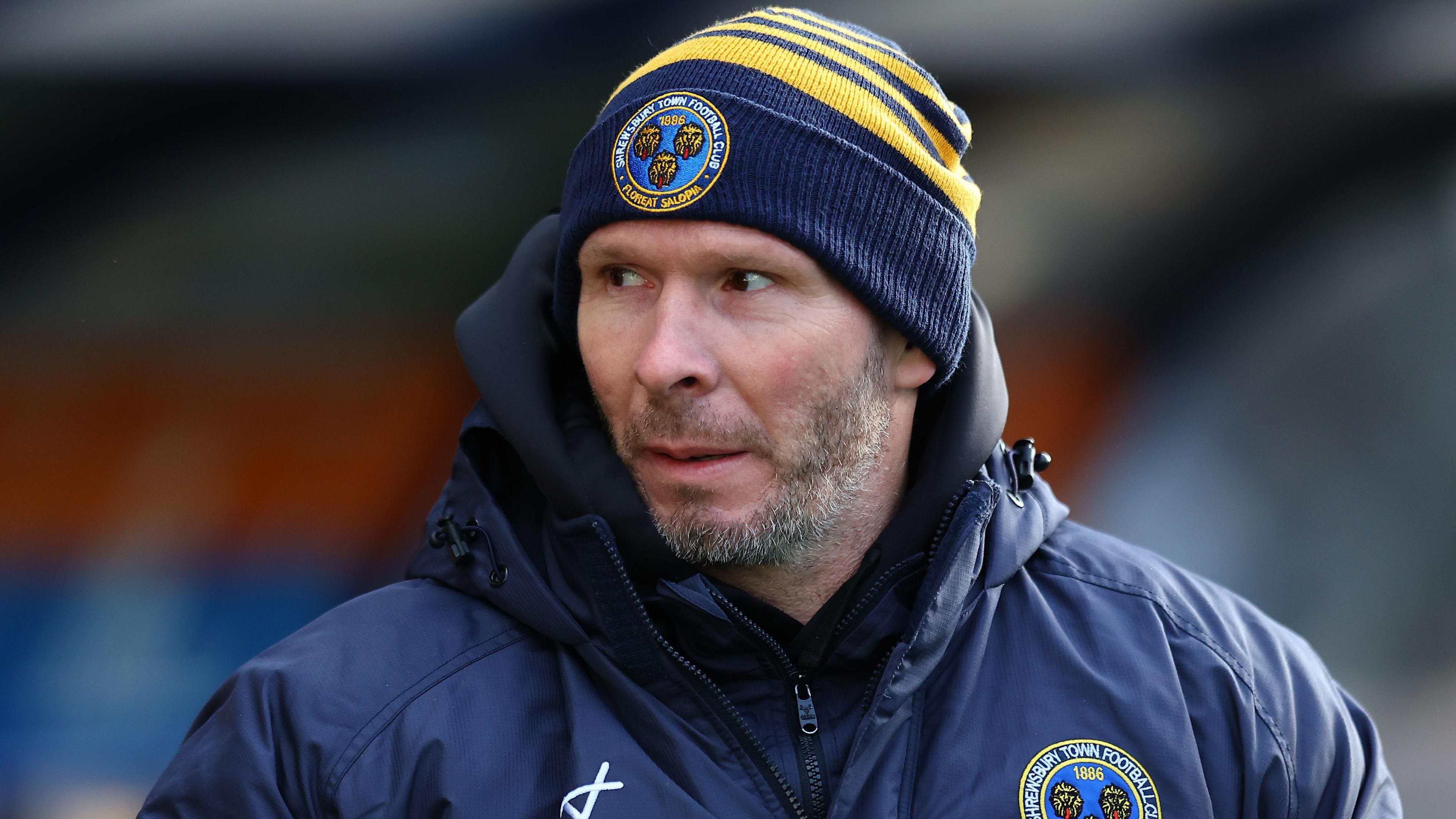 Shrewsbury Town head coach Michael Appleton watches on in his club coat and beanie