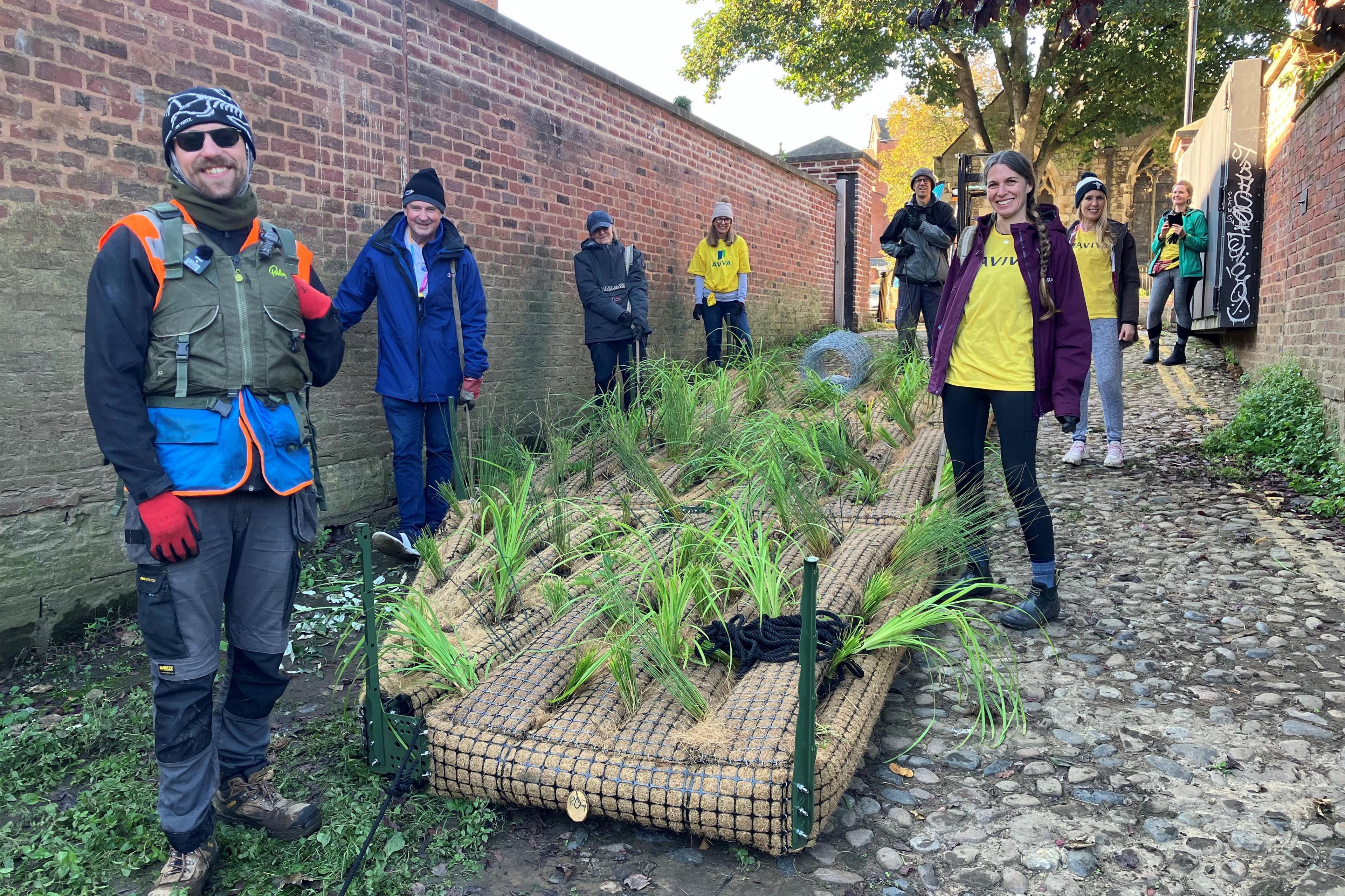 Volunteers standing by a pontoon-like structure with vegetation planted in it