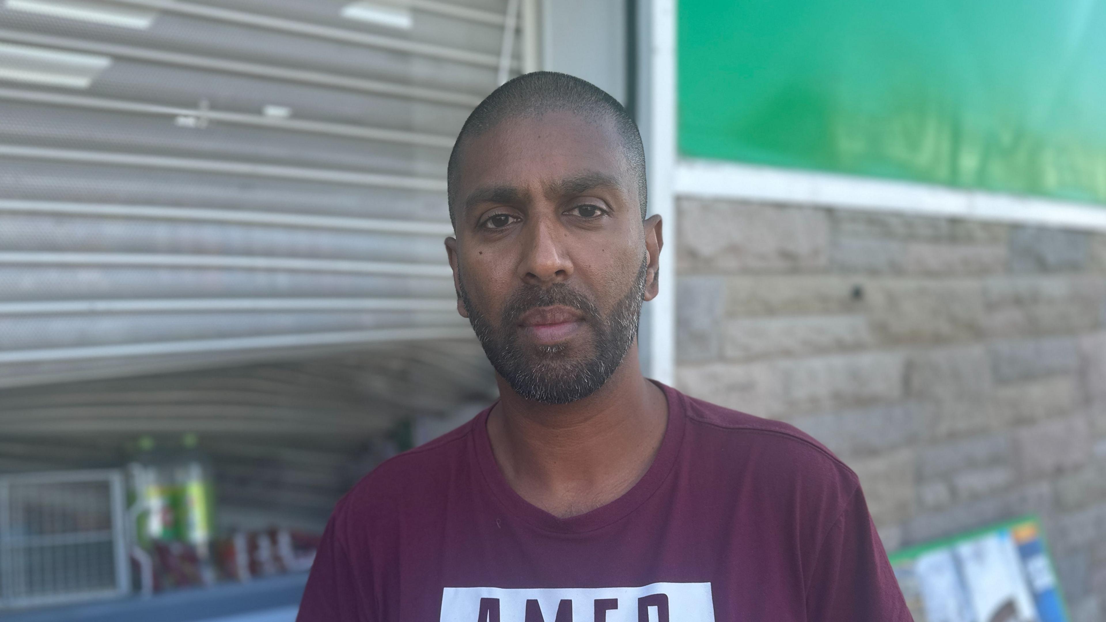 Shopkeeper Chanaka Balasuryla standing in front of a damaged security door at his cornershop in Southport