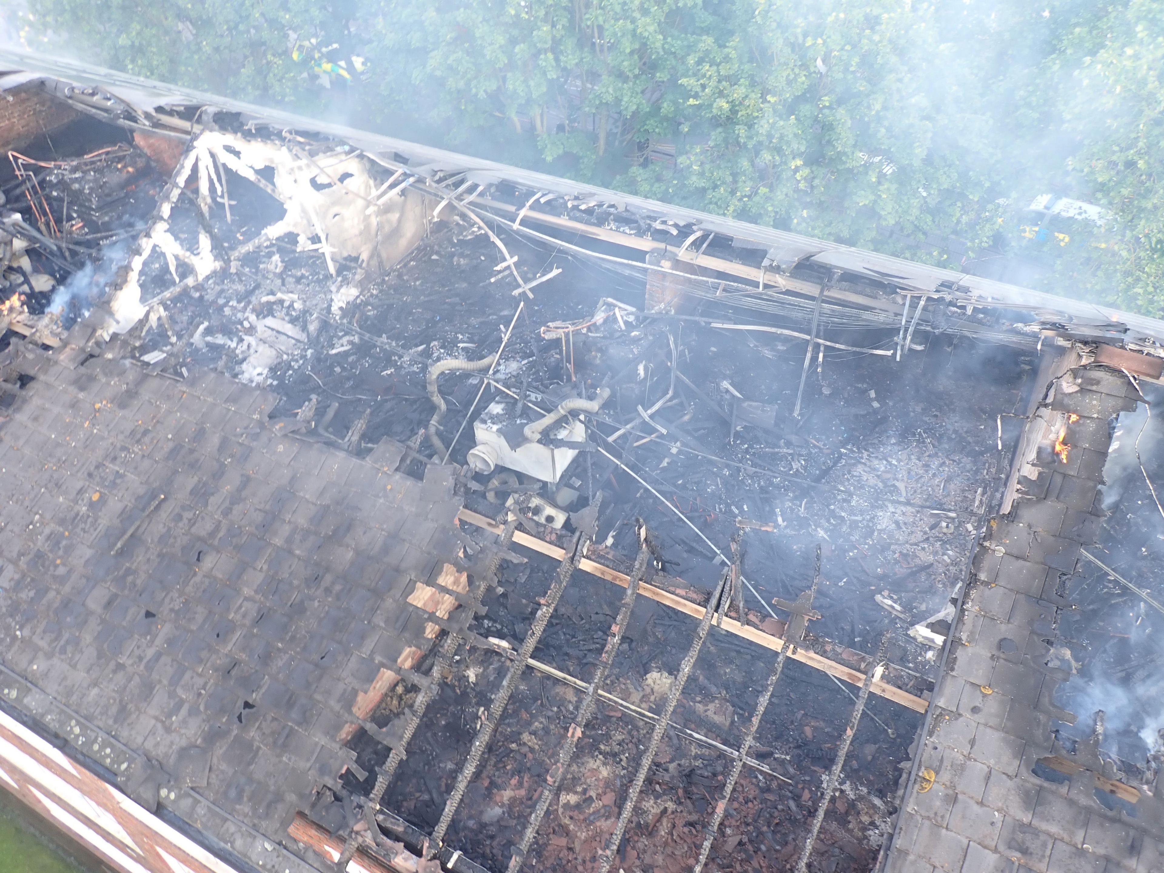 Aerial view of damaged roof of black of flats with smoke rising