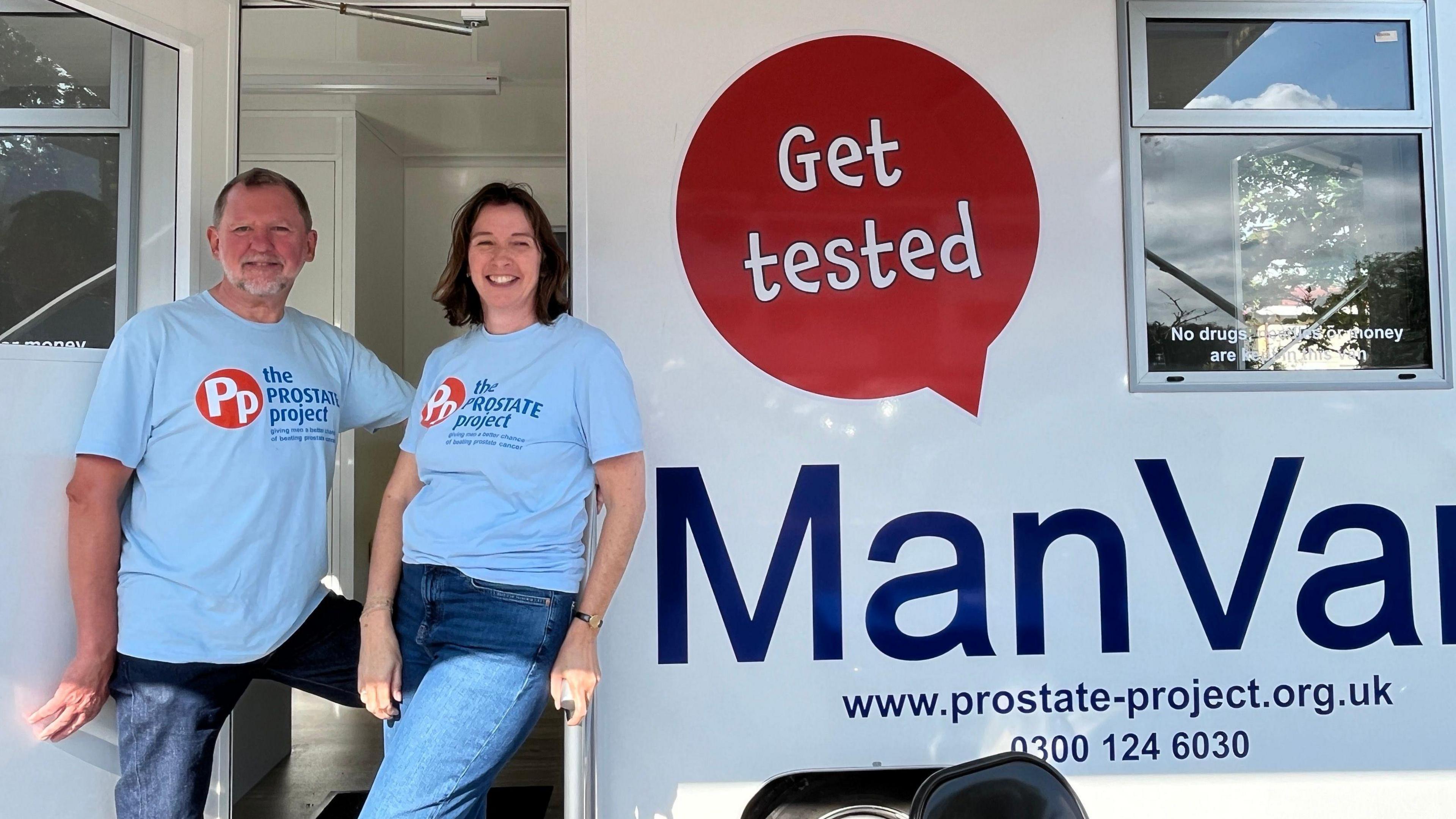 A man and woman, both dressed in blue t-shirts with The Prostate Project on them, stand in front of a van